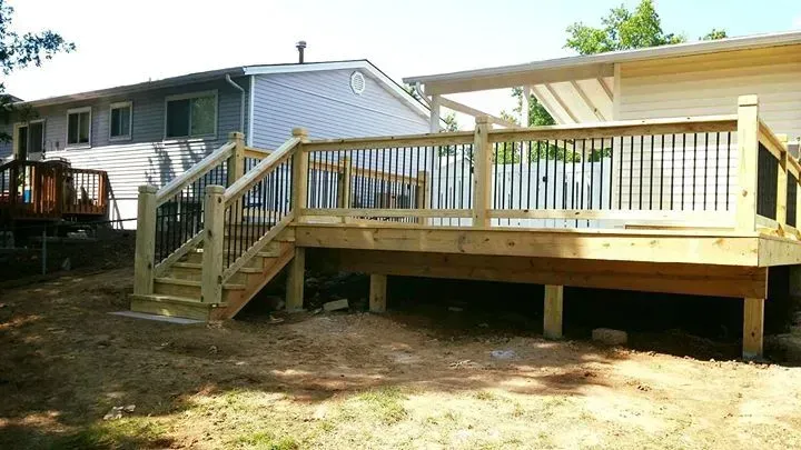 A wooden deck with stairs leading up to it is in the backyard of a house.