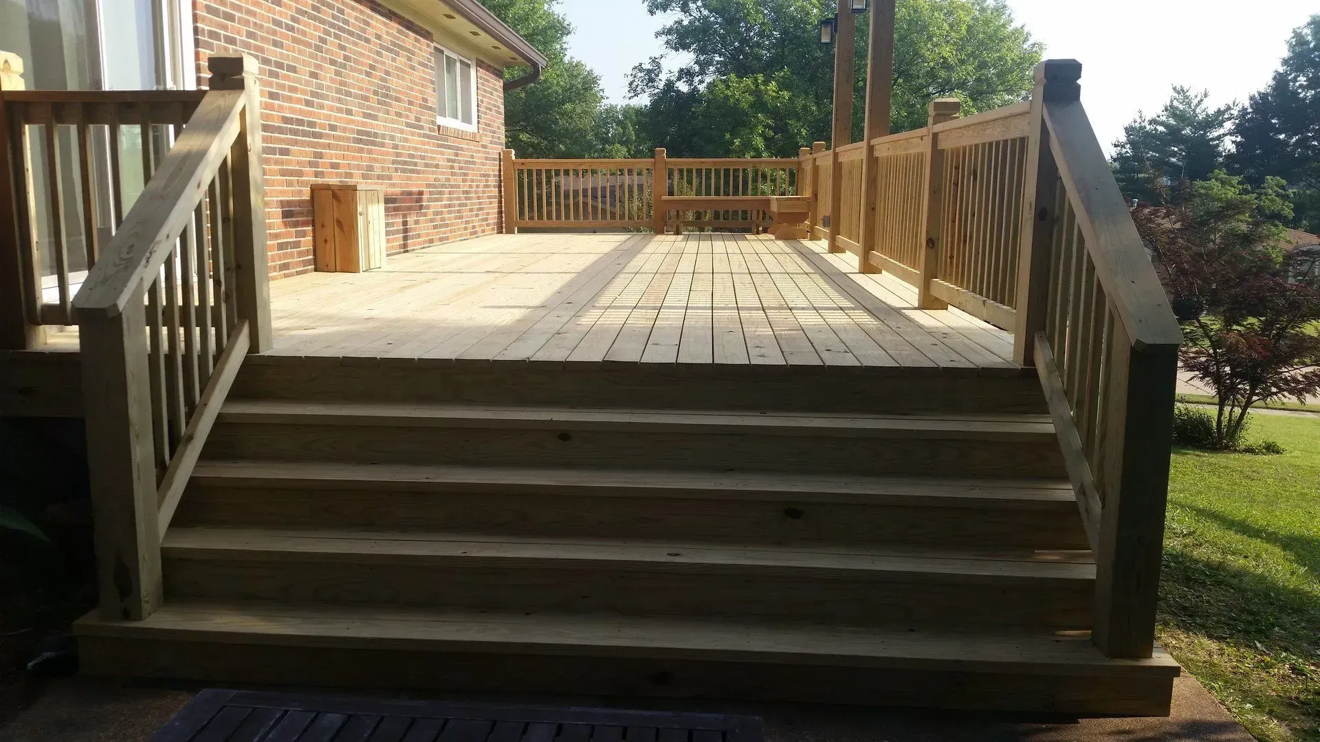 A wooden deck with stairs leading up to it and a brick house in the background.
