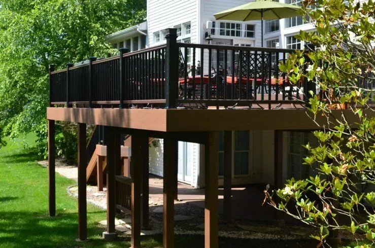 A large wooden deck with a black railing and umbrellas in front of a house.