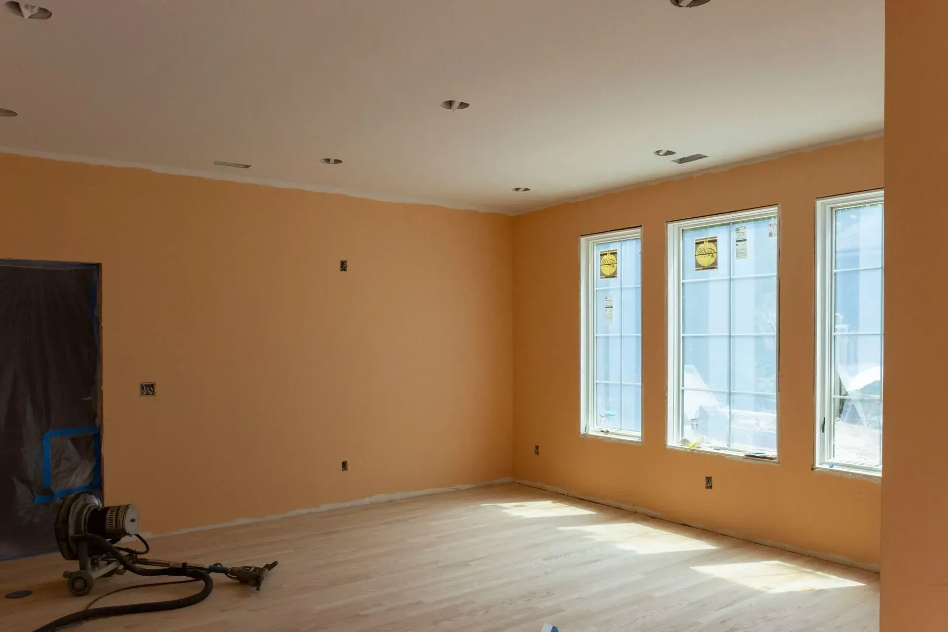 An empty room with three windows and a vacuum cleaner on the floor.