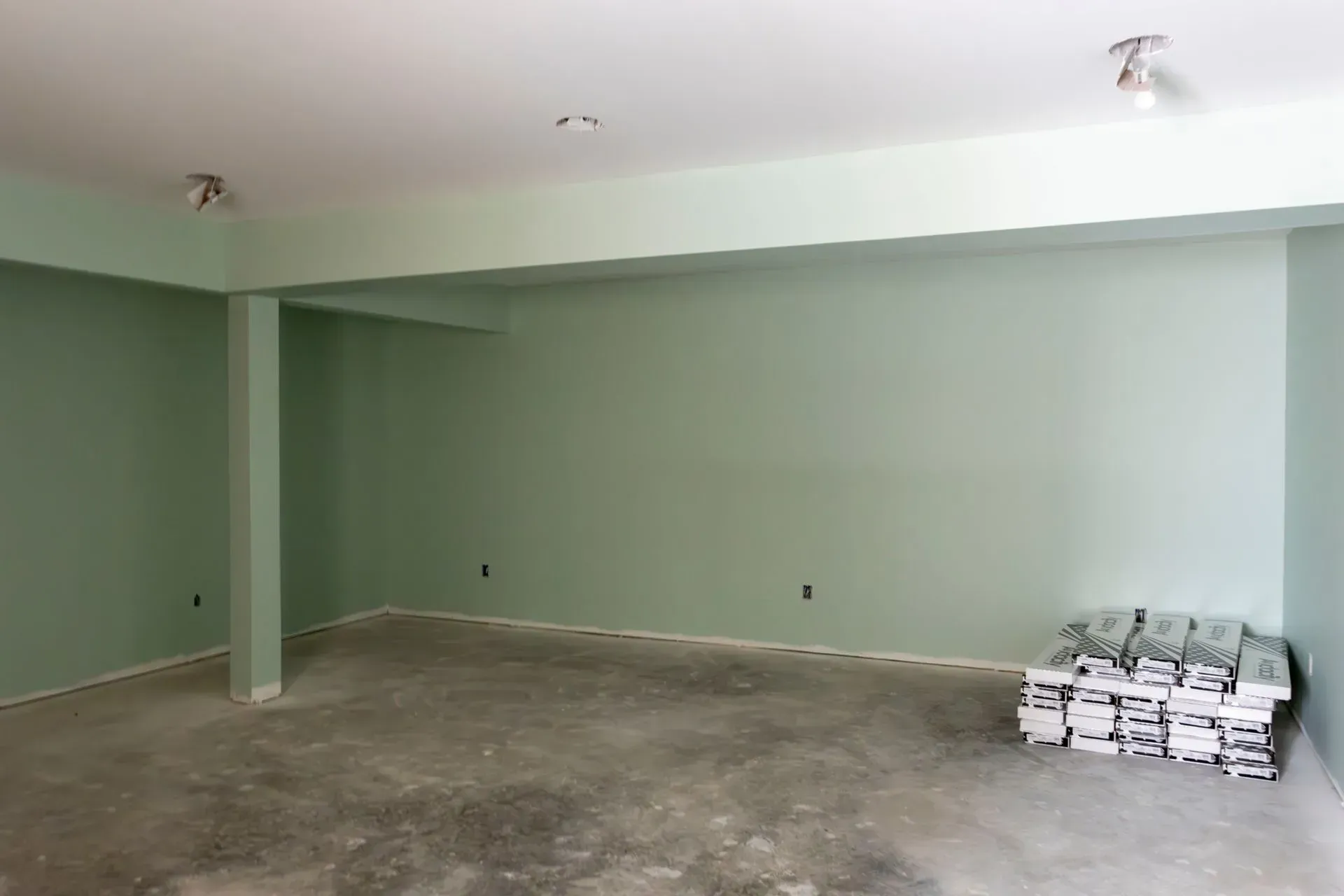 An empty room with green walls and a stack of boxes on the floor.