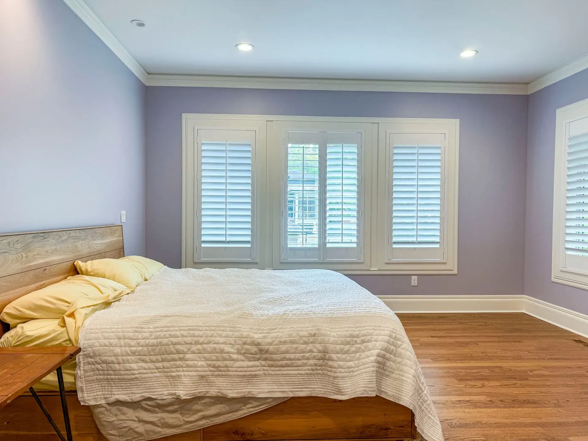 A bedroom with purple walls and white shutters on the windows.