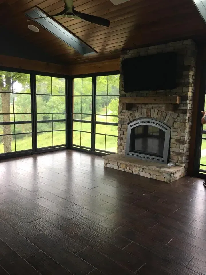 A screened in porch with a fireplace and a flat screen tv.