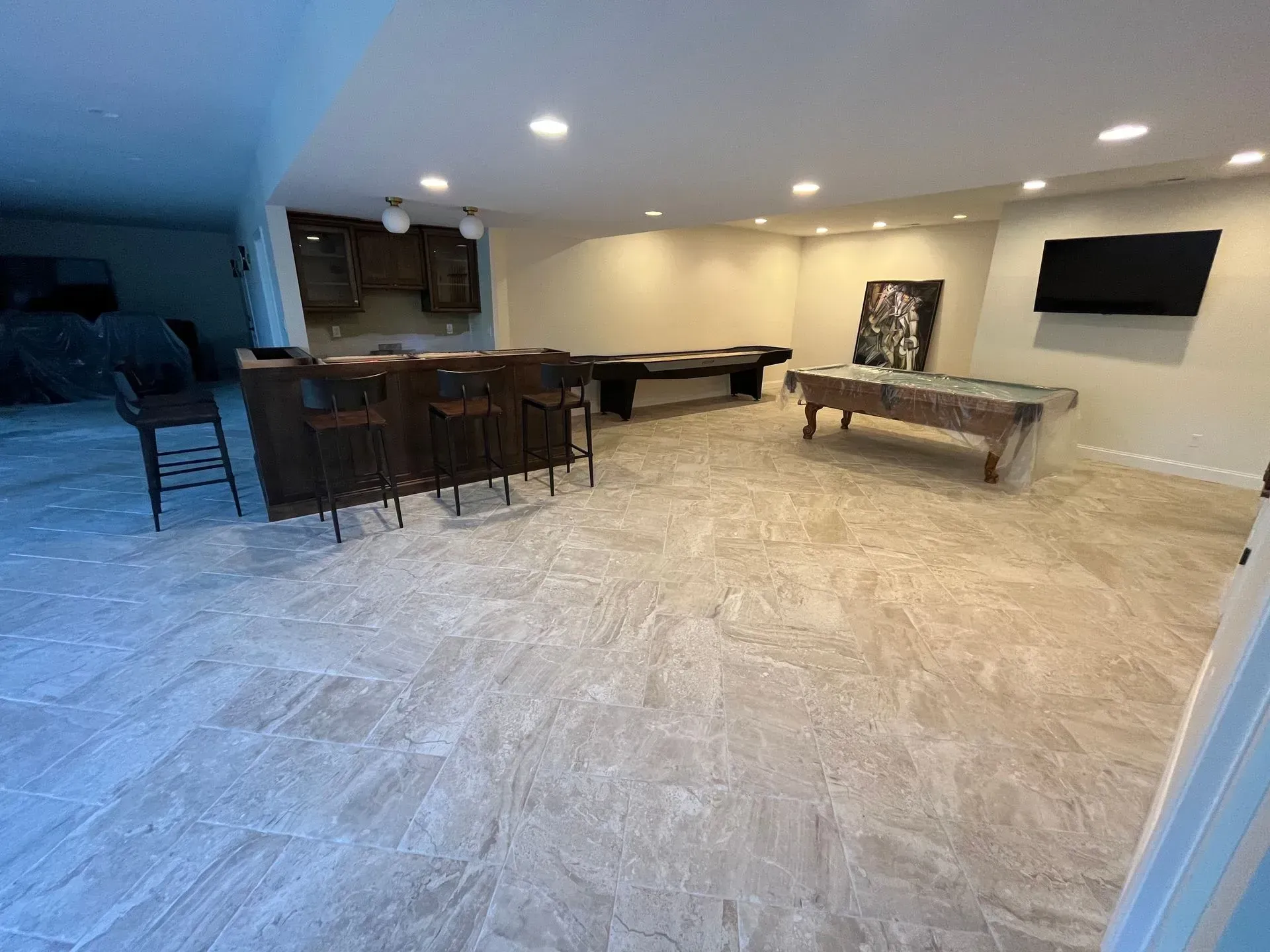 A basement with a pool table, bar, and television.