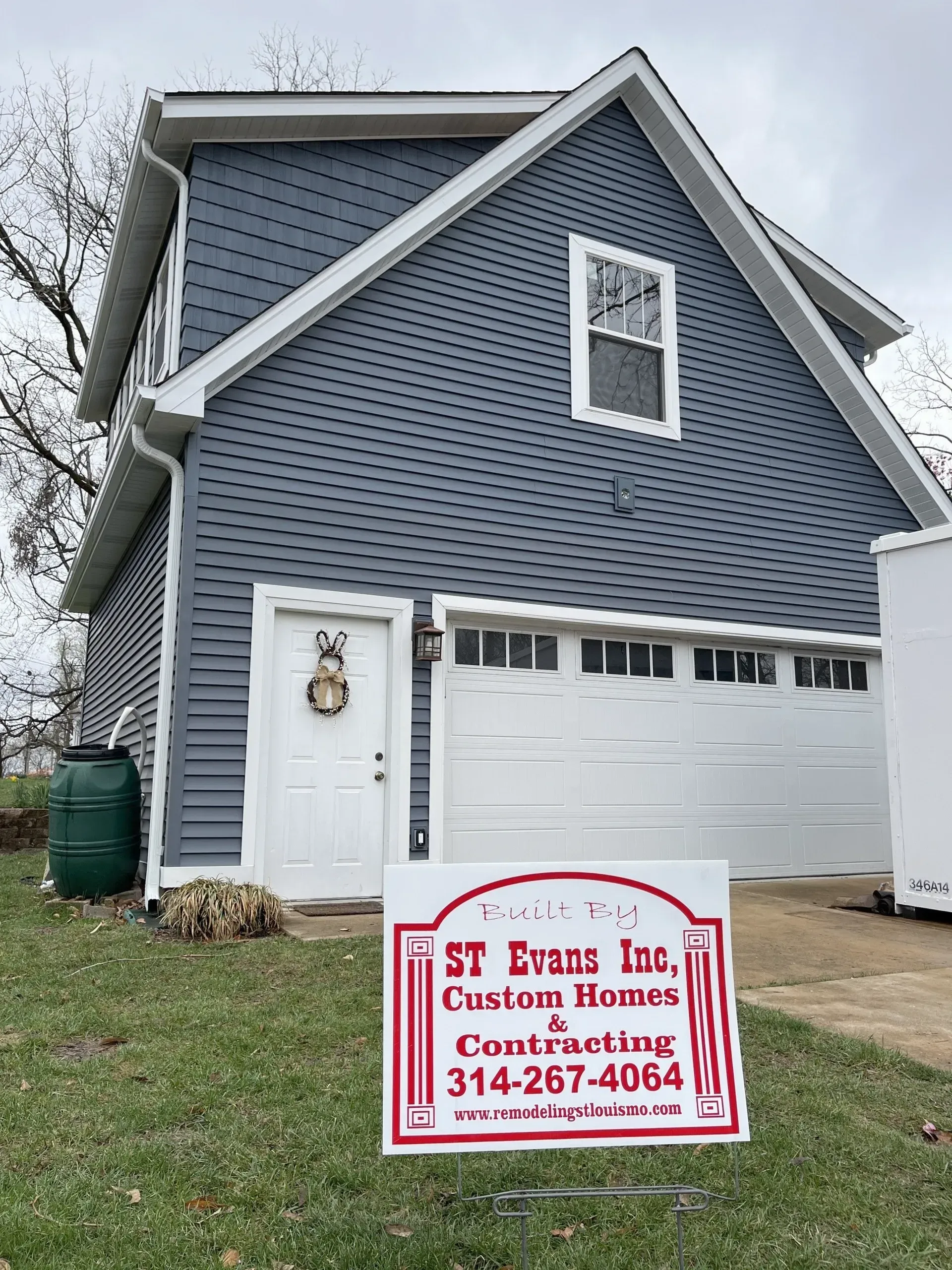 A blue house with a white garage door and a sign in front of it.
