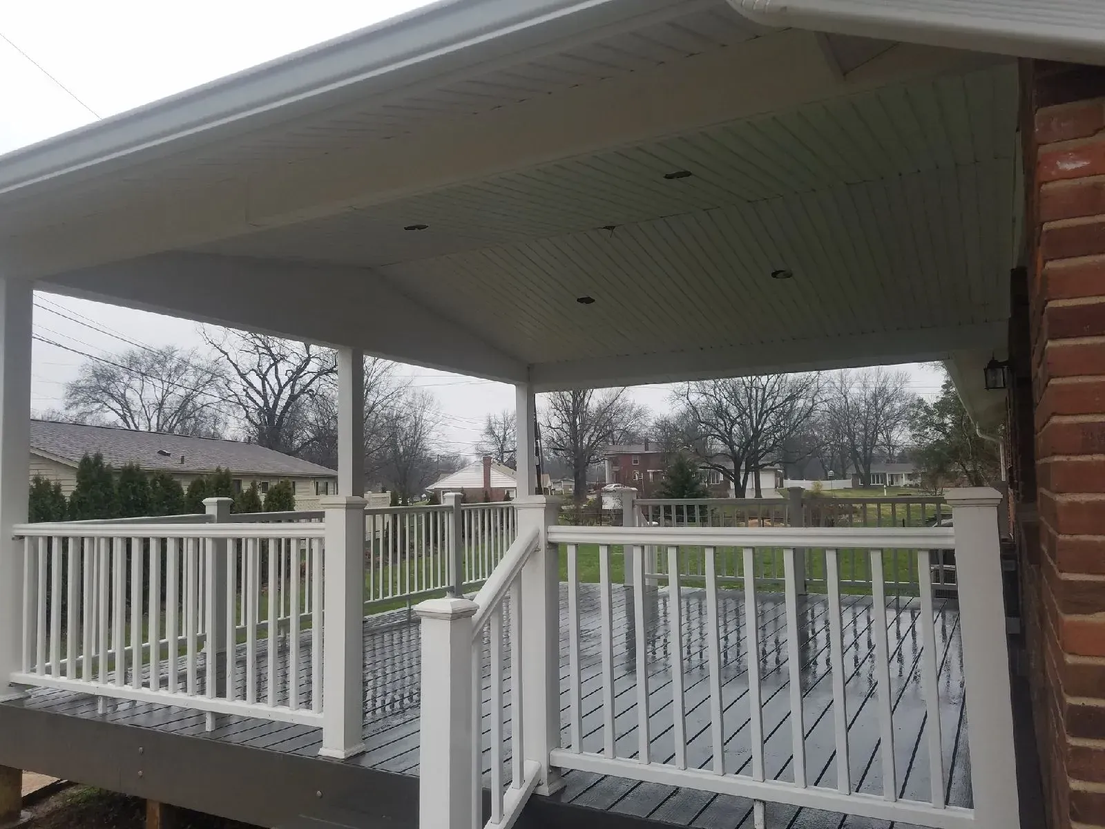 A porch with a white railing and a brick house in the background