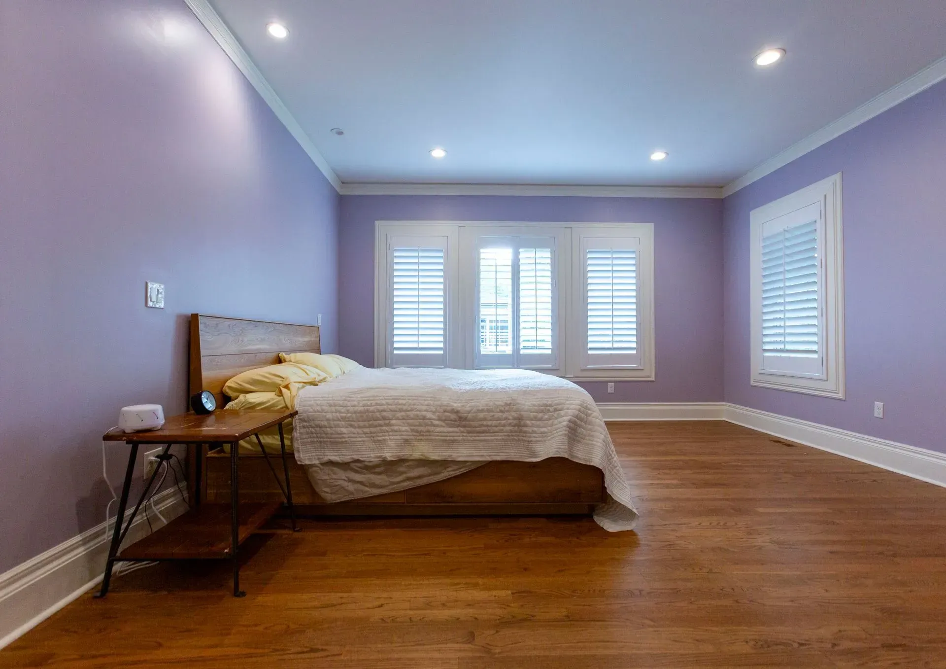 A bedroom with purple walls and hardwood floors and a bed.