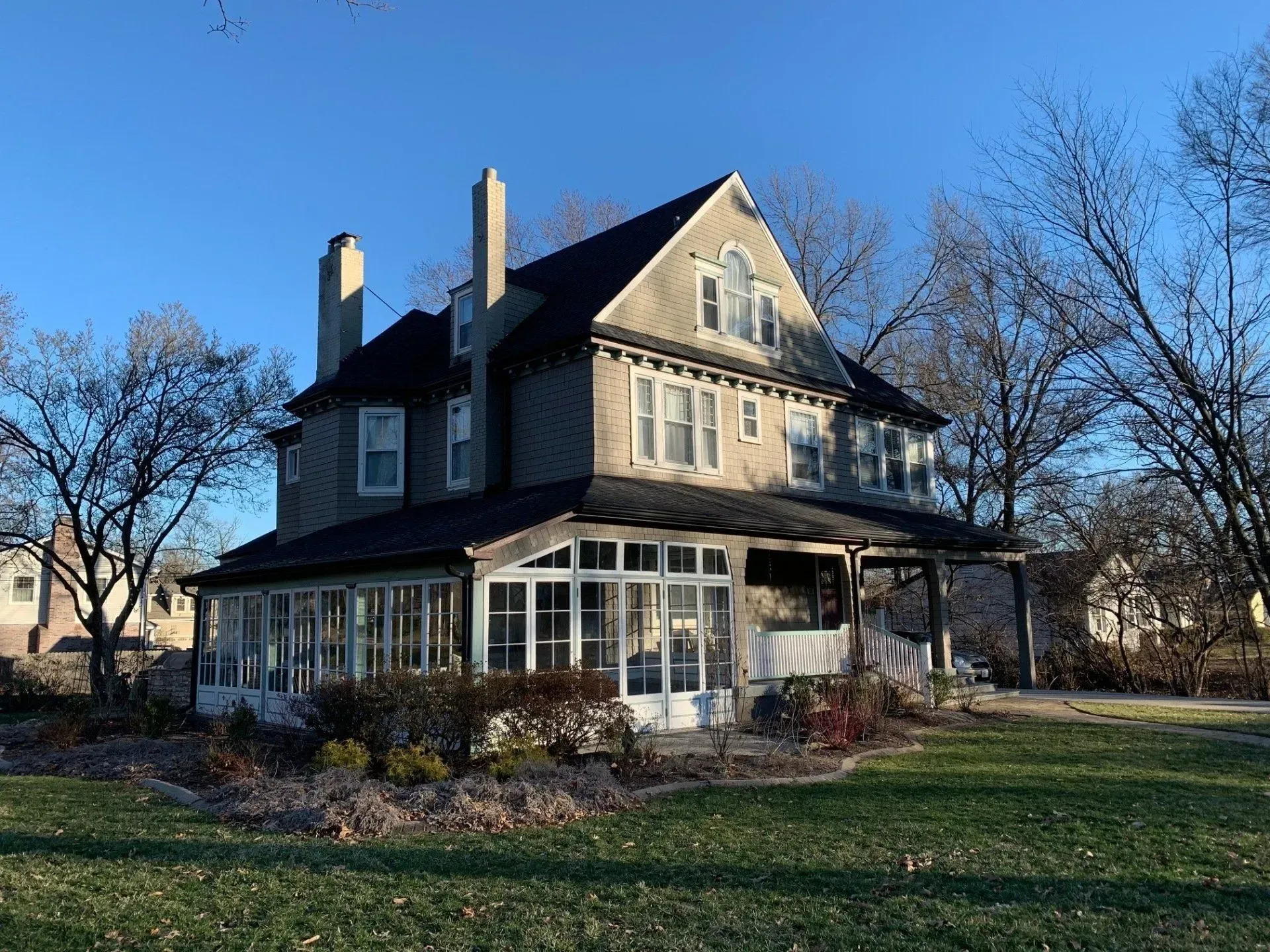 A large house with a large porch is sitting on top of a lush green field.