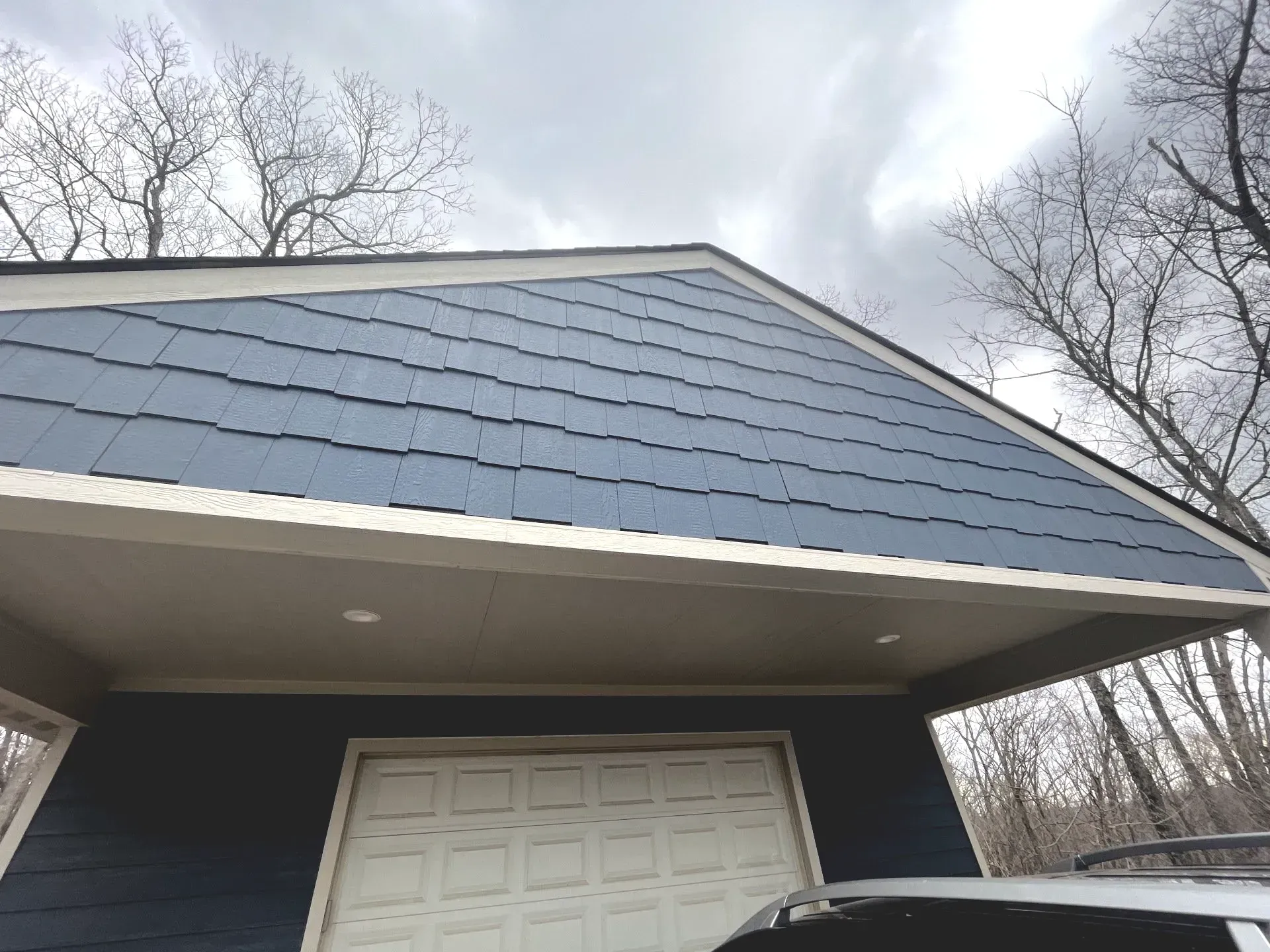 A blue garage with a white door and a car parked underneath it.