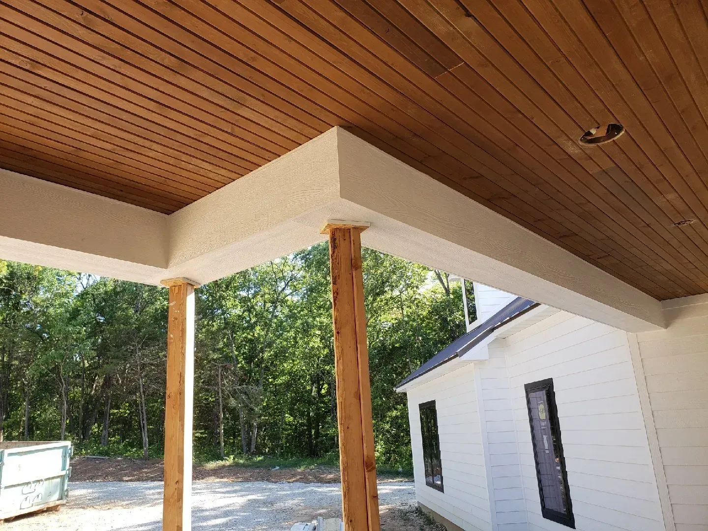 A porch with a wooden ceiling and a white house in the background.