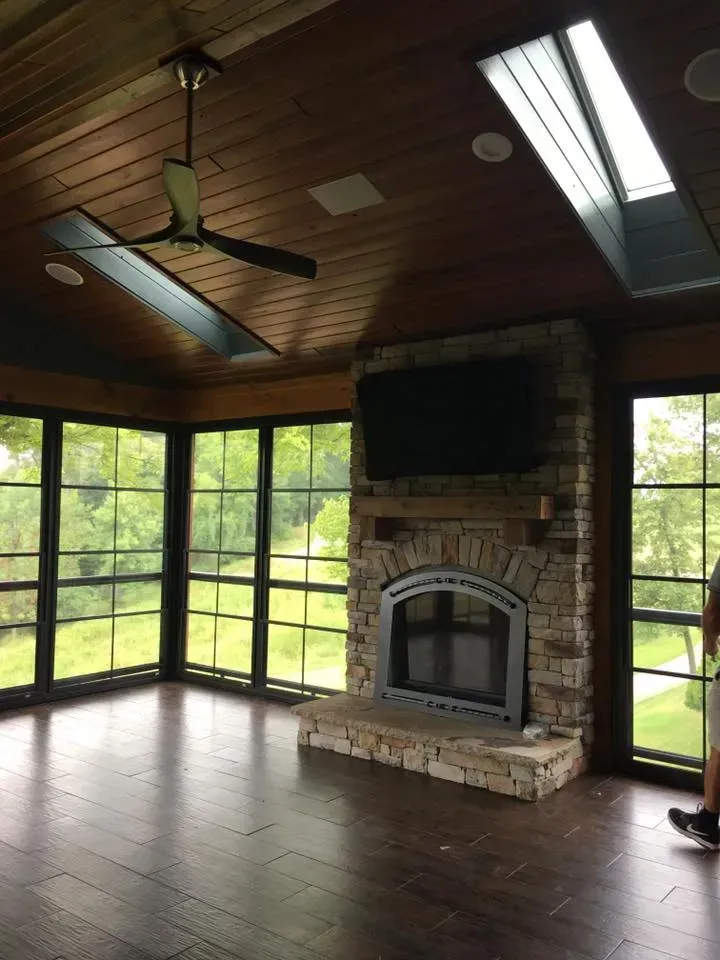 A screened in porch with a fireplace and a flat screen tv