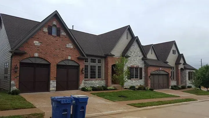 A row of houses with garages and trash cans in front of them.