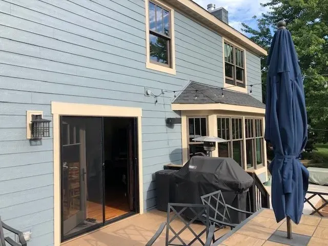 The back of a house with a blue umbrella and a grill