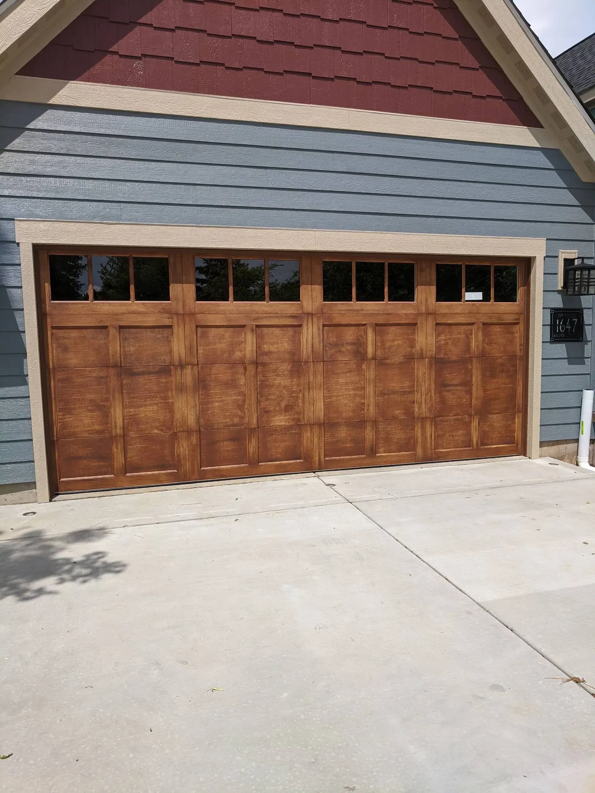 A large wooden garage door is in front of a blue house