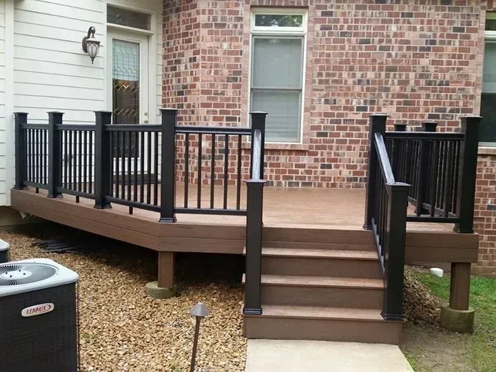 A deck with stairs and a black railing in front of a brick house.