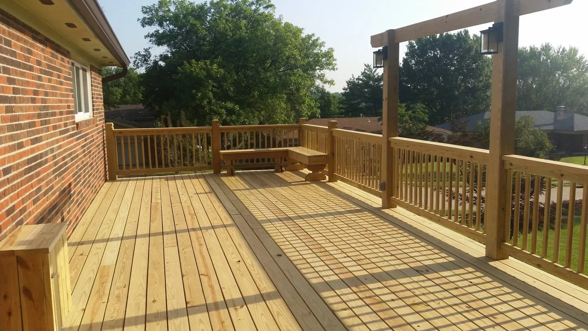 A large wooden deck with a brick house in the background