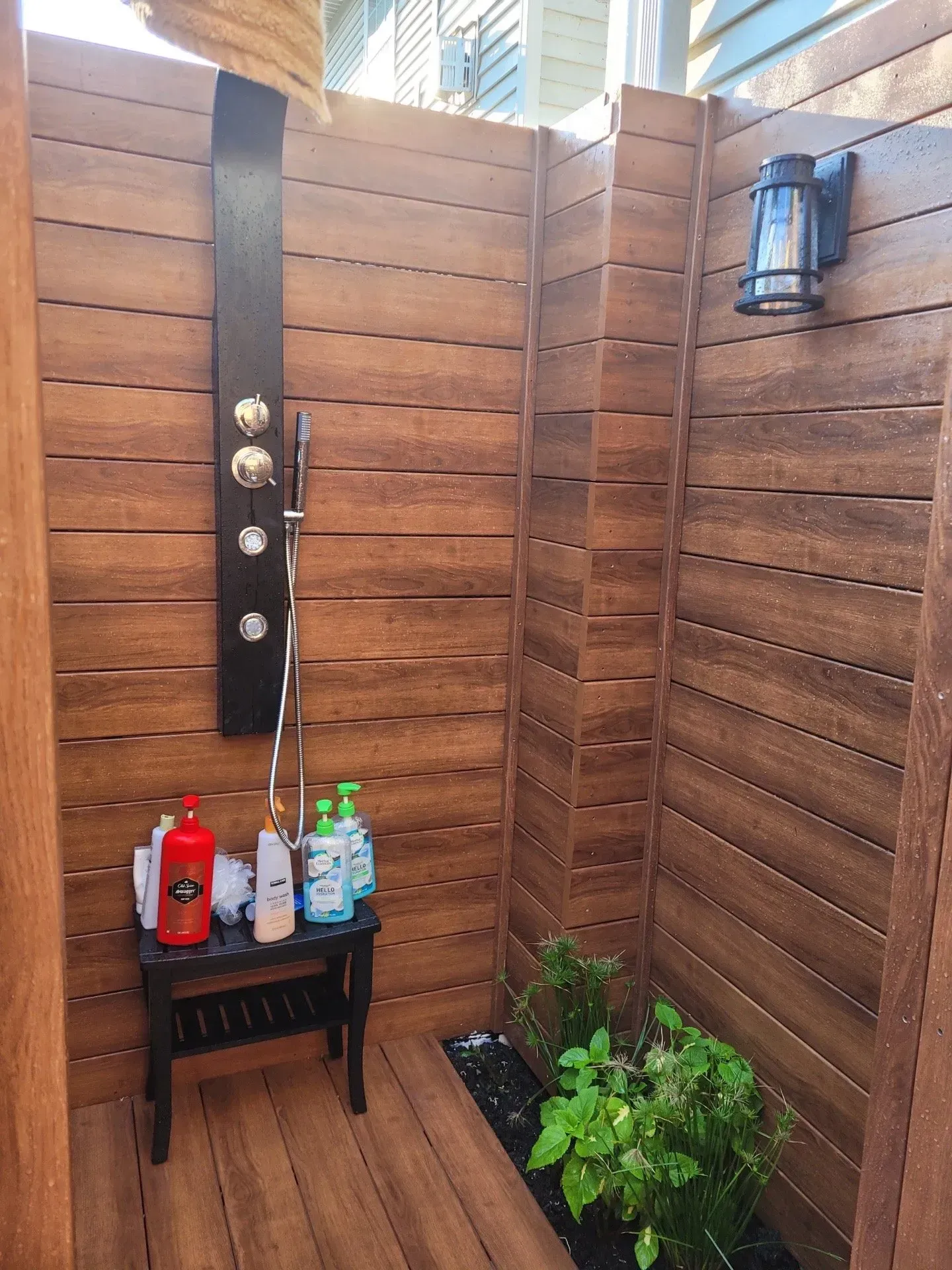 A wooden outdoor shower with bottles of soap on a bench.