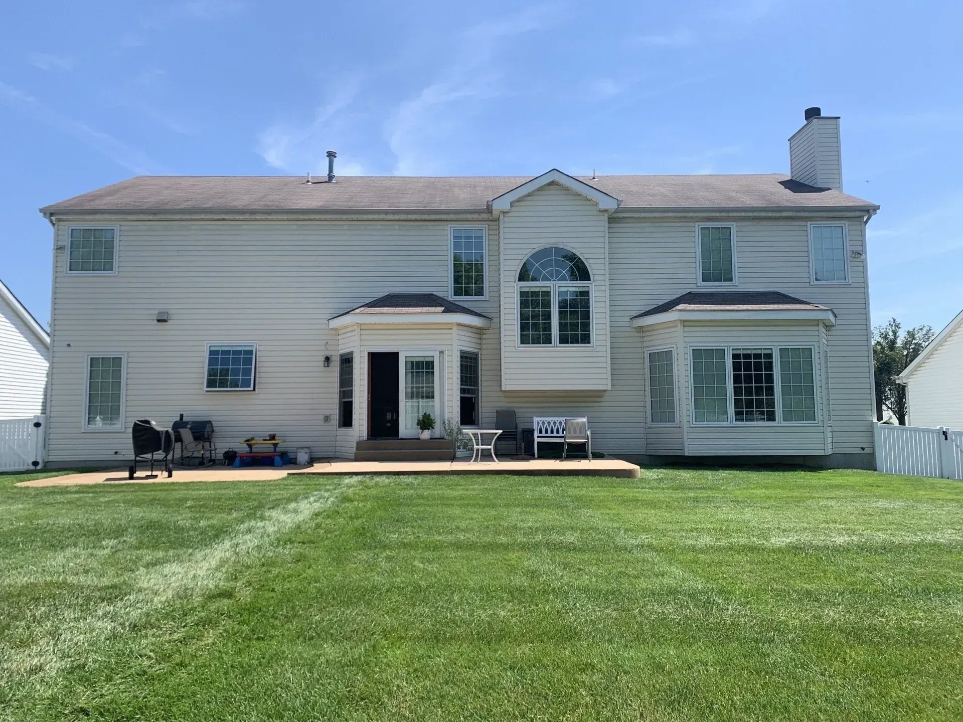 The back of a large white house with a large lawn in front of it.