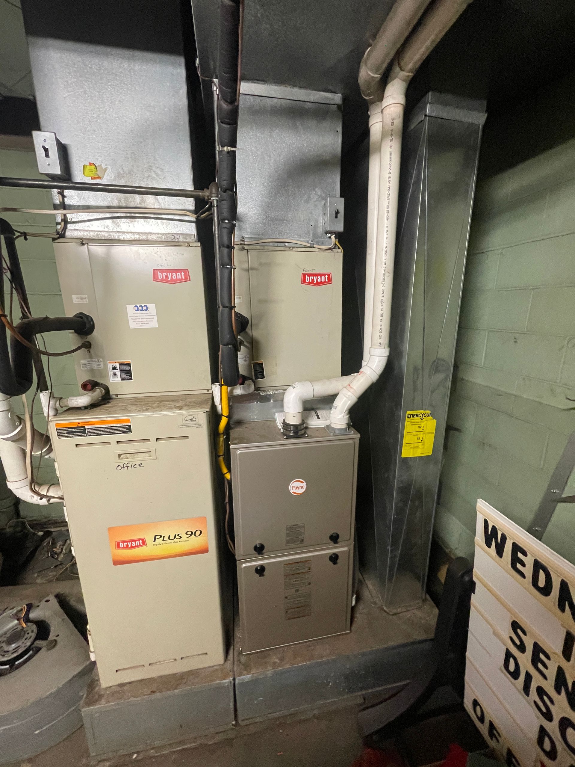 Furnace system in a utility room. Rectangular metal units, ductwork, and pipes. Gray and beige tones.