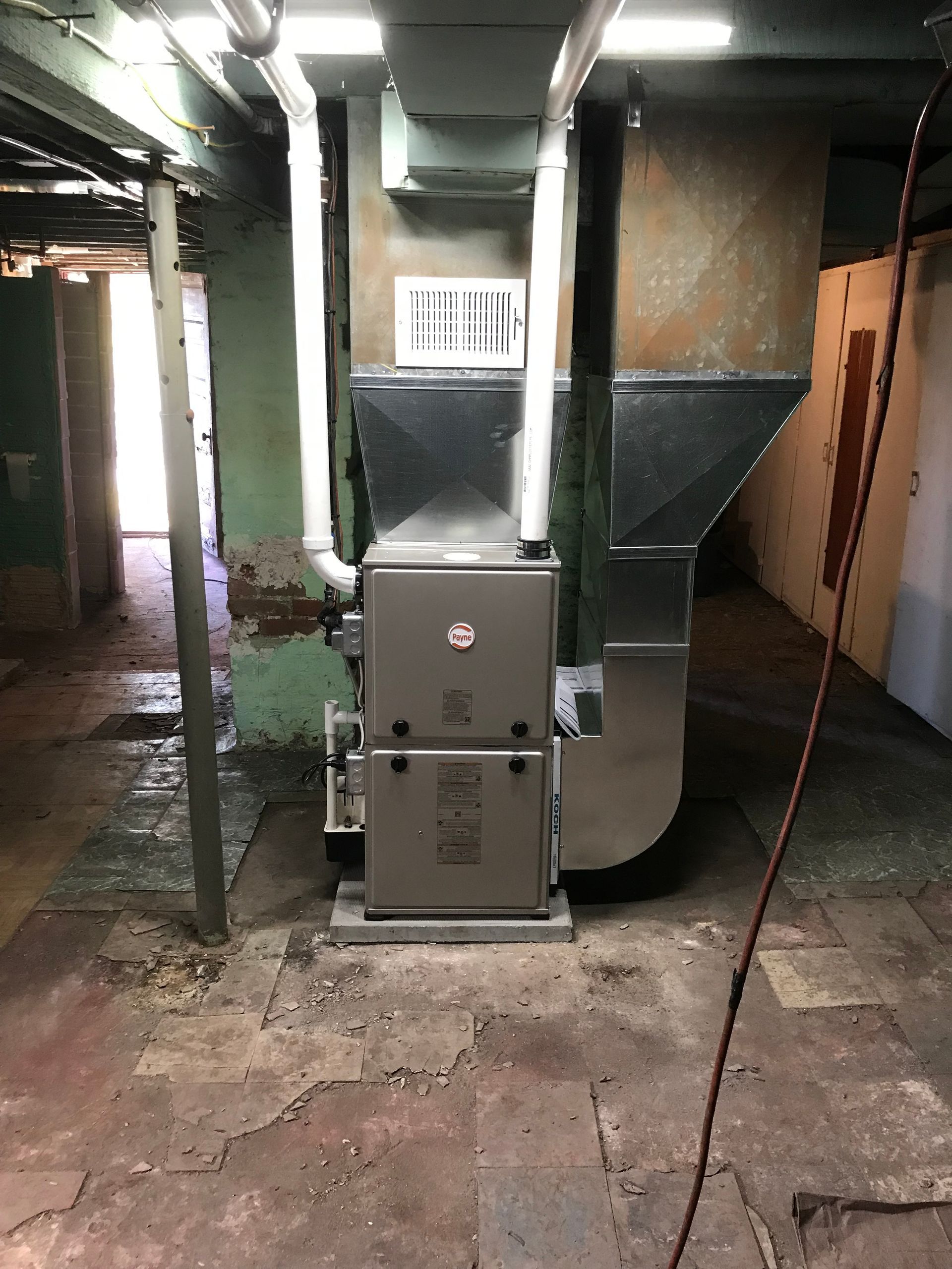 Furnace in a basement. The furnace is a silver box with a vent on top. Dark basement with concrete floor.