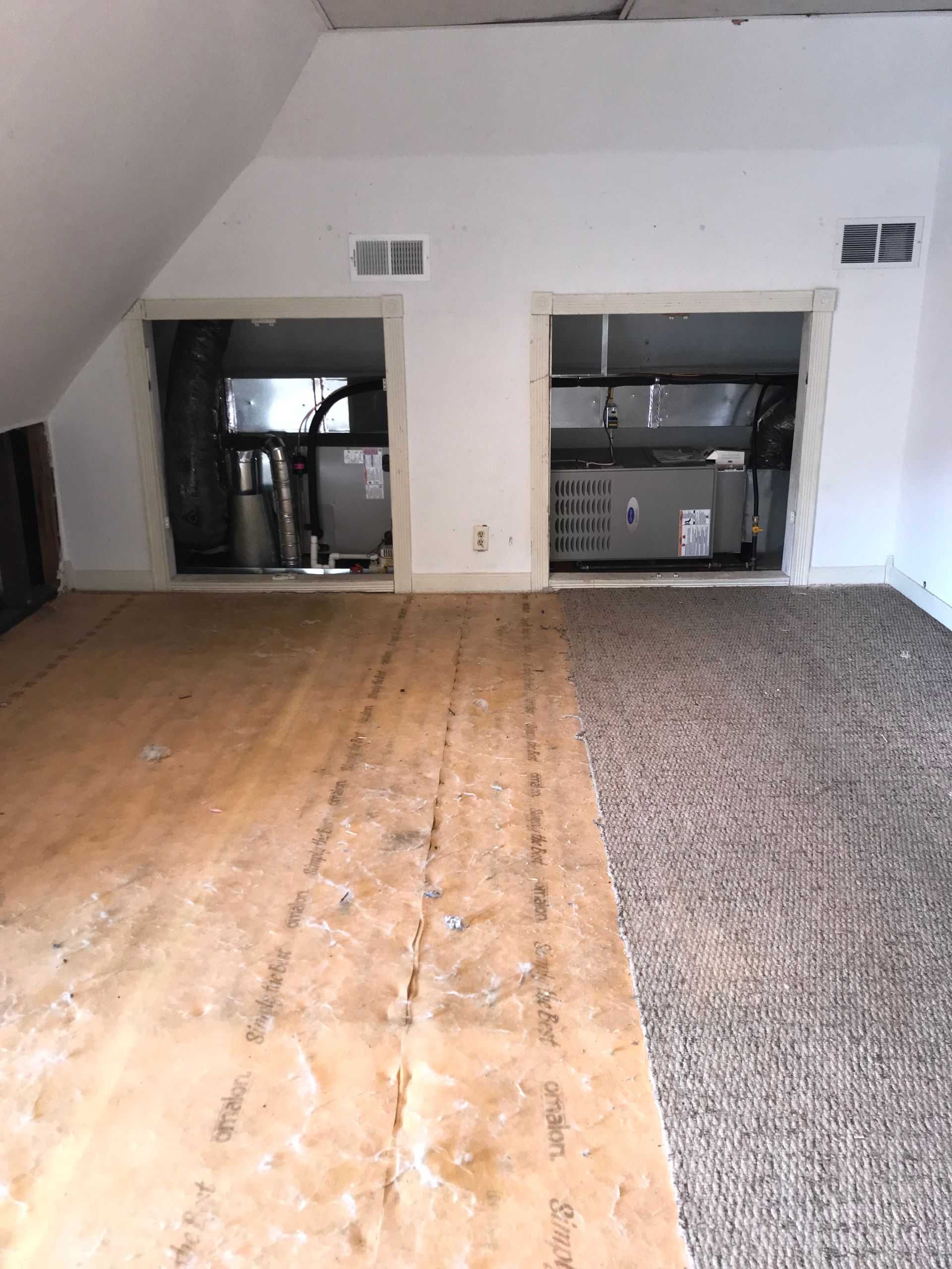 Attic with exposed floorboards and carpeting. Two HVAC units are visible in recessed wall openings.