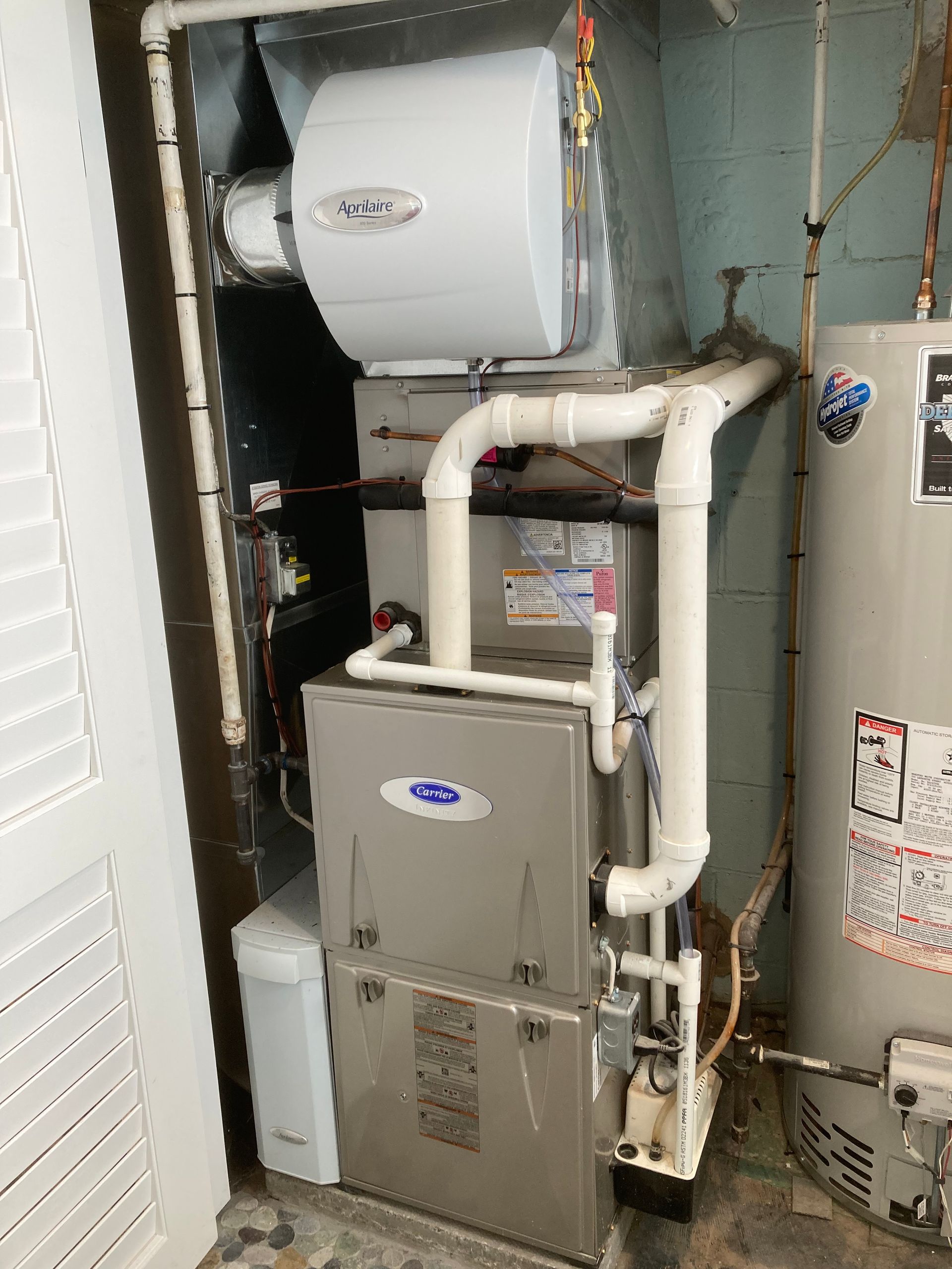 Furnace and humidifier unit in a basement, connected to white PVC pipes and a hot water heater.