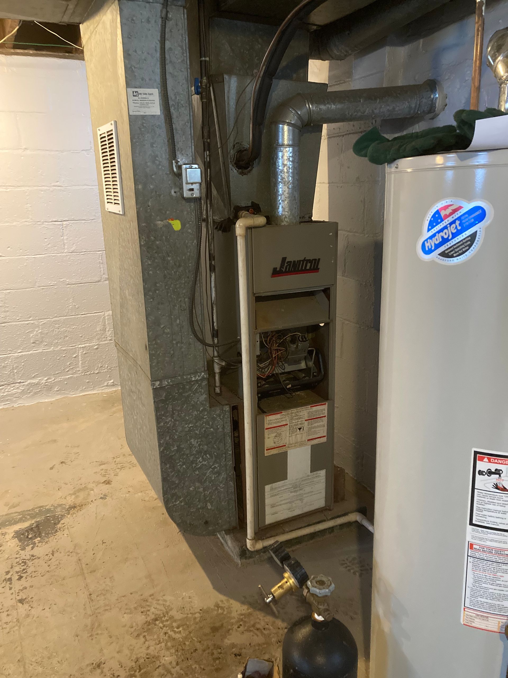 Furnace and water heater in a basement. Grey furnace, silver water heater, and a gray concrete wall.