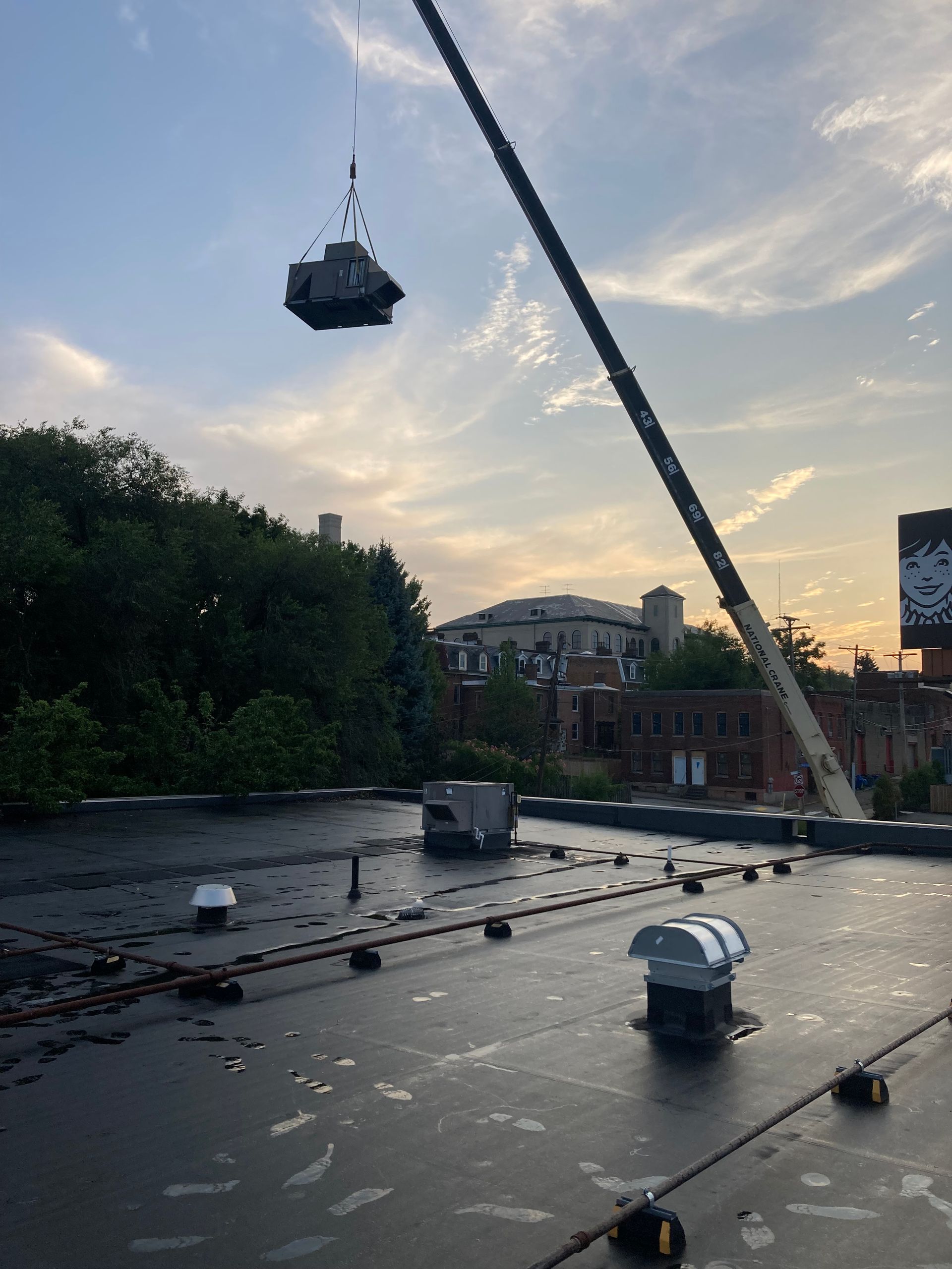 A crane lifting a large, square object over a city rooftop.