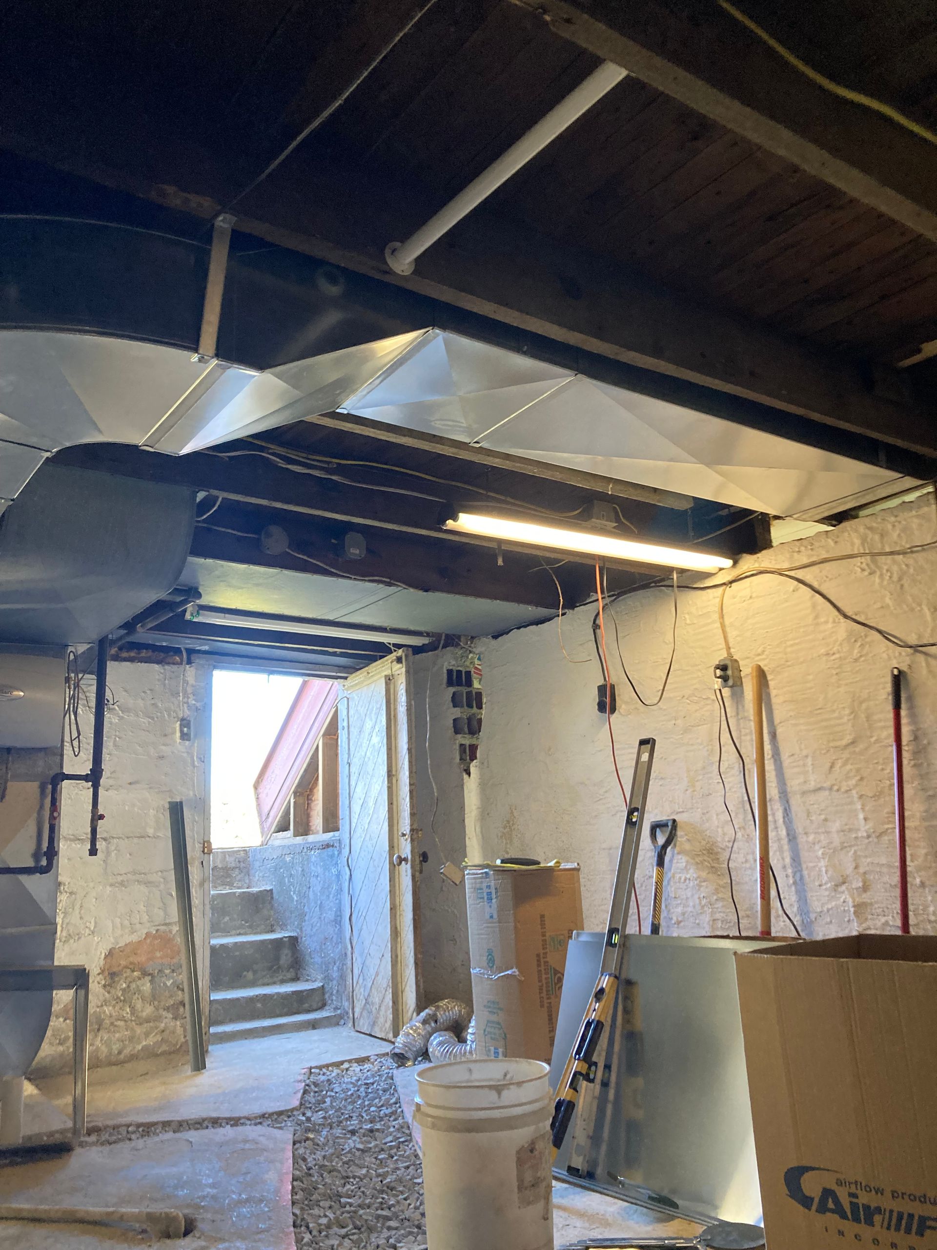 Basement interior with ductwork, exposed beams, and concrete stairs leading outside.