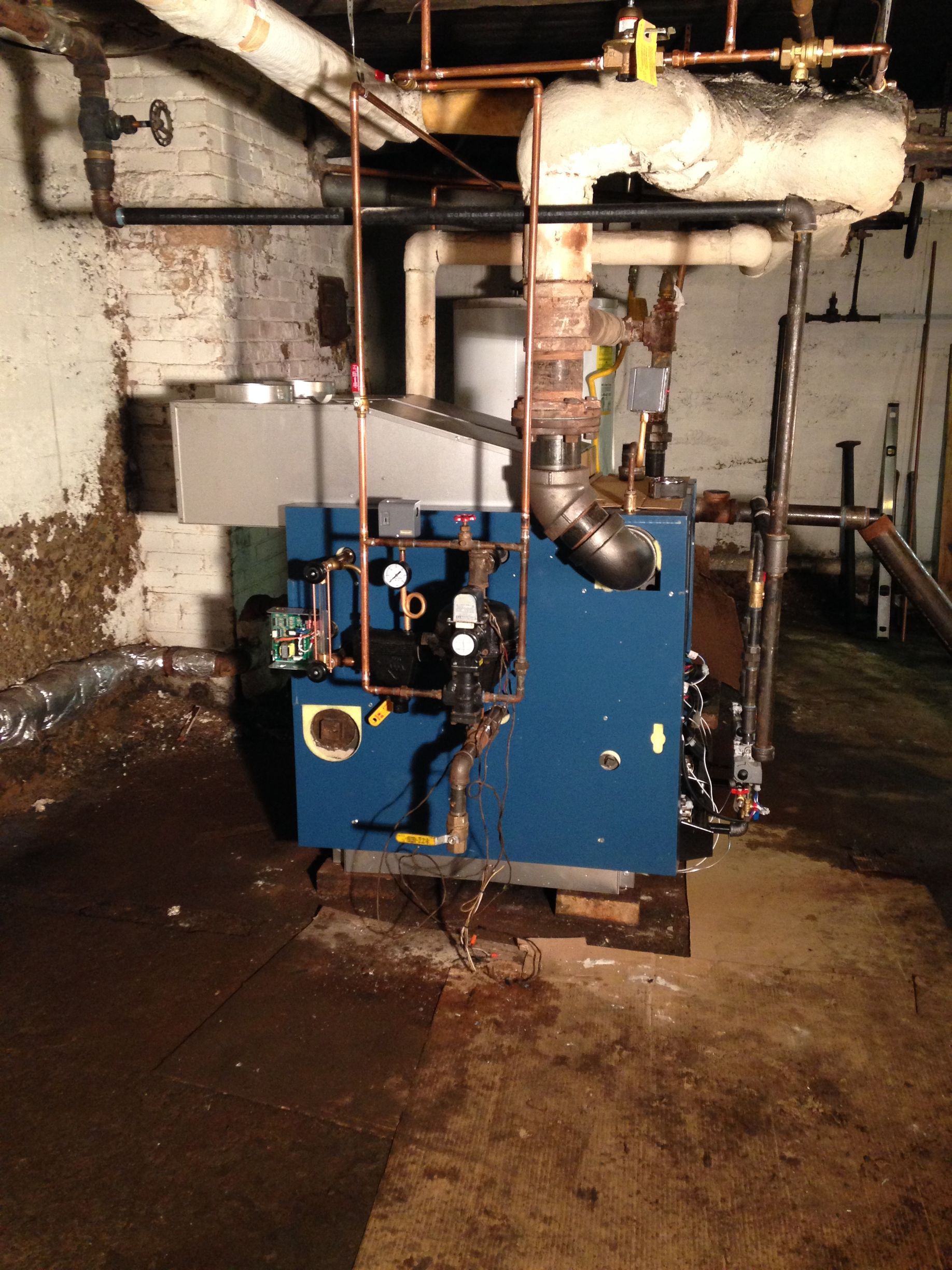 Blue boiler in a utility room with pipes and wiring. Brown and white walls.