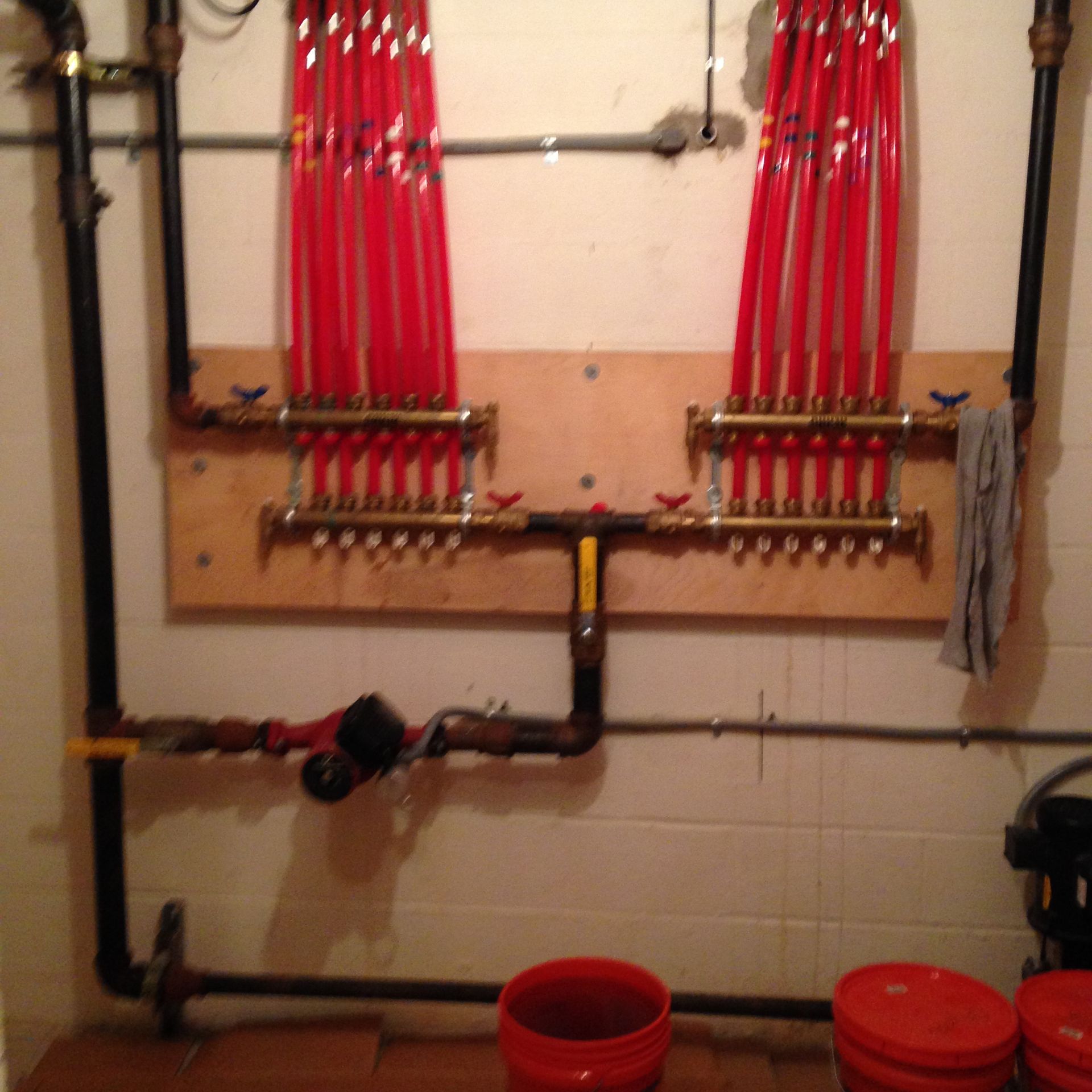 Hydronic radiant floor heating system with red tubing, pipes, and valves mounted on a wooden board.