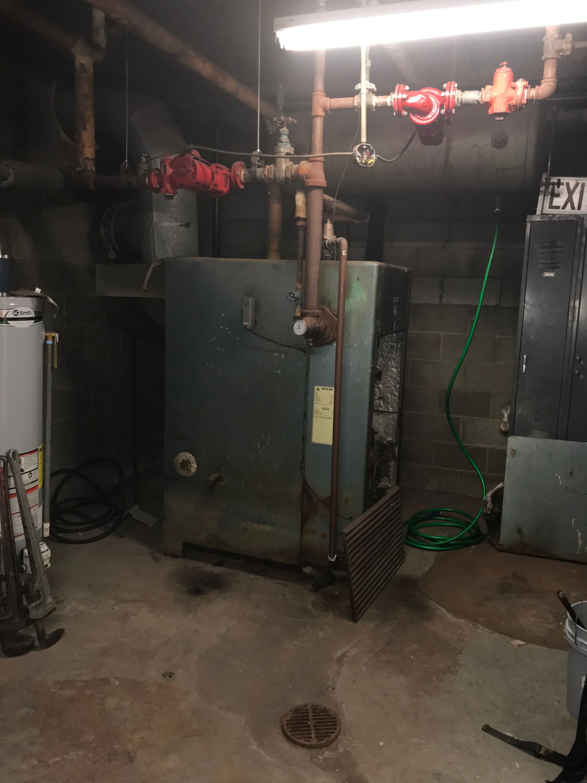 Old boiler in a basement, with pipes and brick walls.