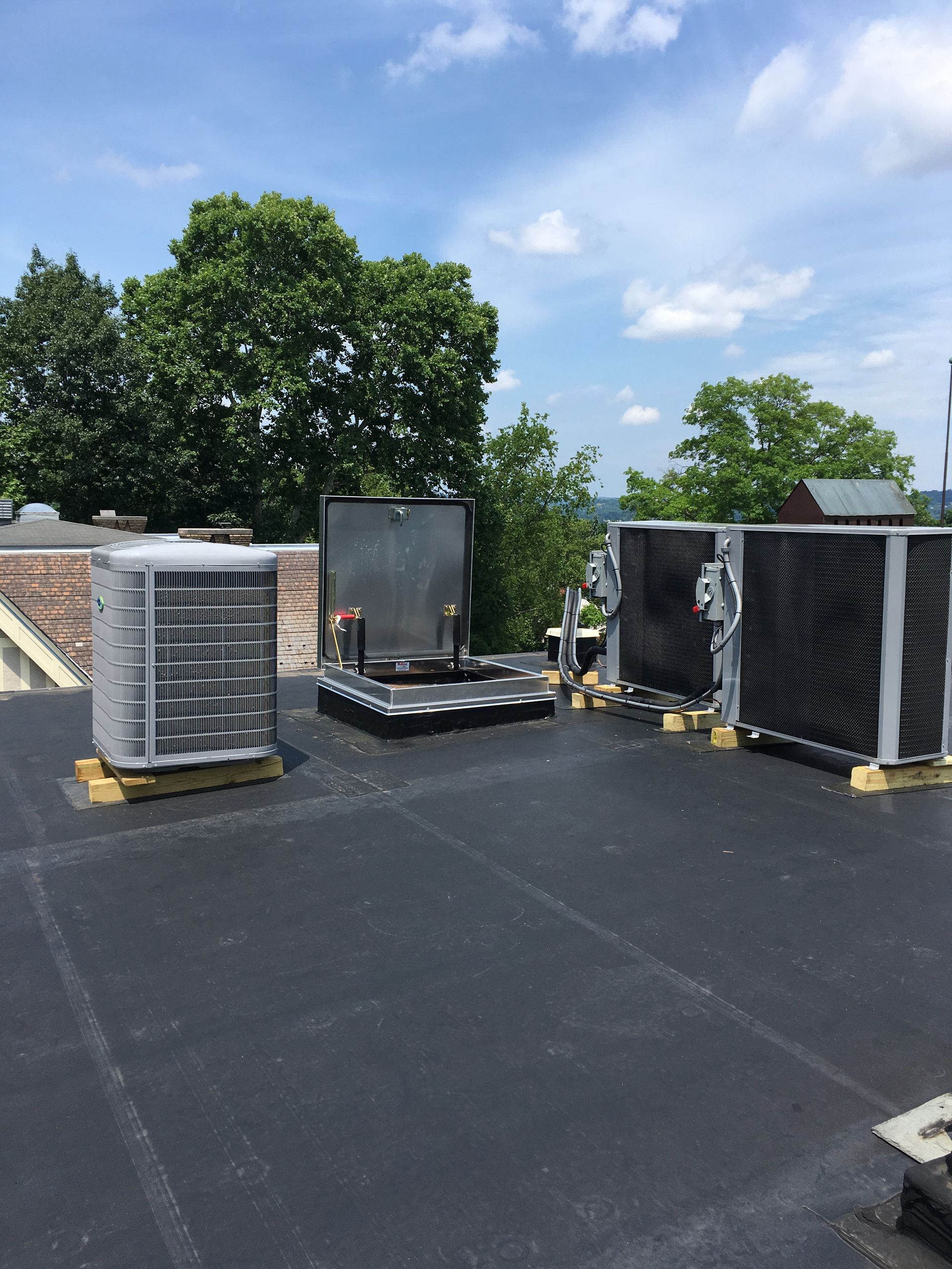 Air conditioning units on a flat roof, blue sky, trees in the background.