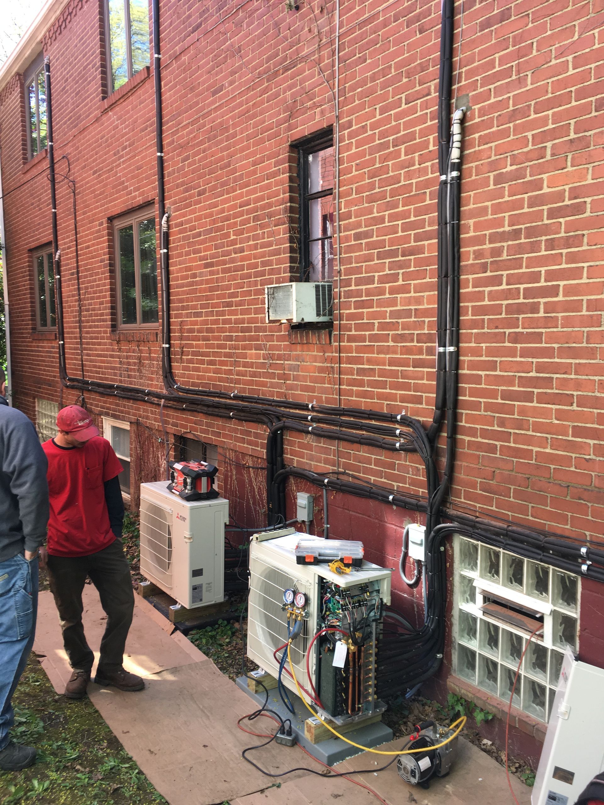 Exterior view of HVAC units and wiring on brick building with workers nearby.
