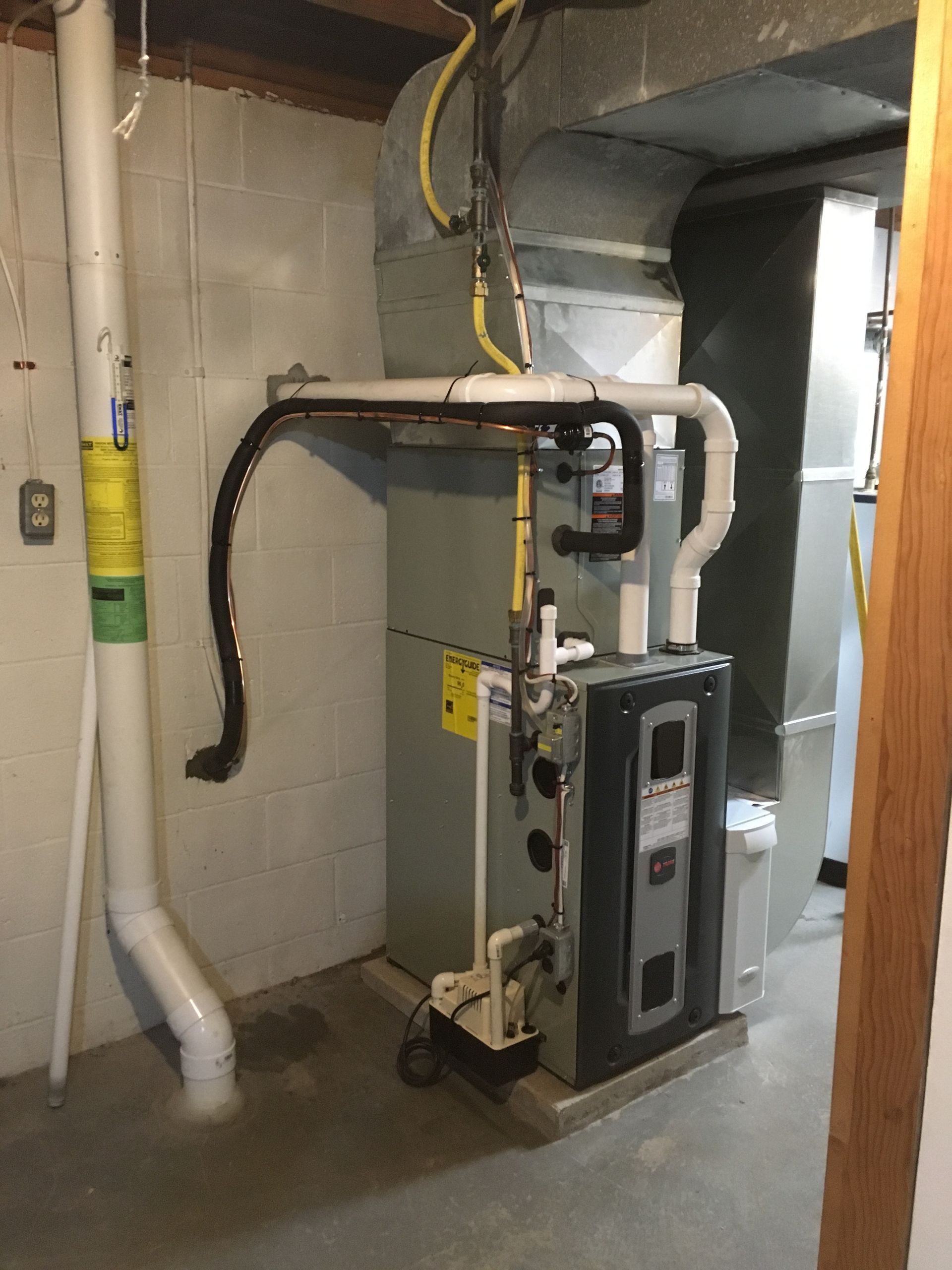Furnace in a basement; gray metal, white pipes, and yellow wires.