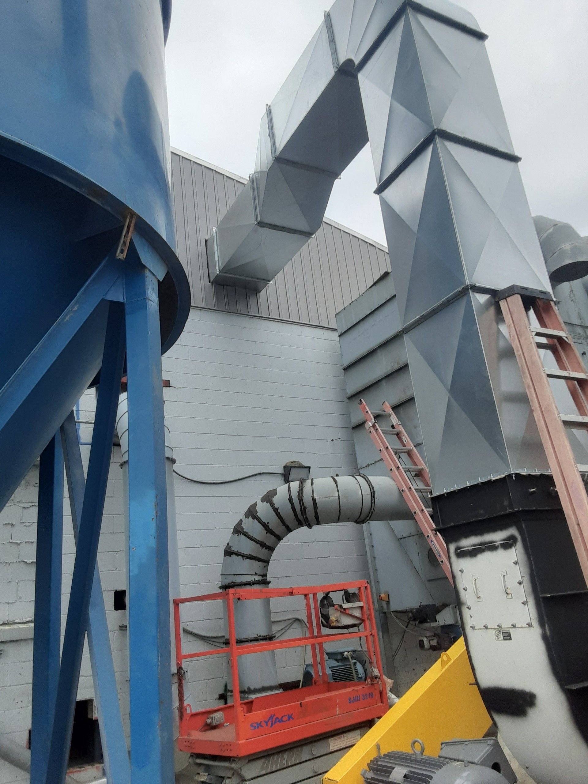 Industrial building exterior with blue silo, metal ductwork, and lift in front.