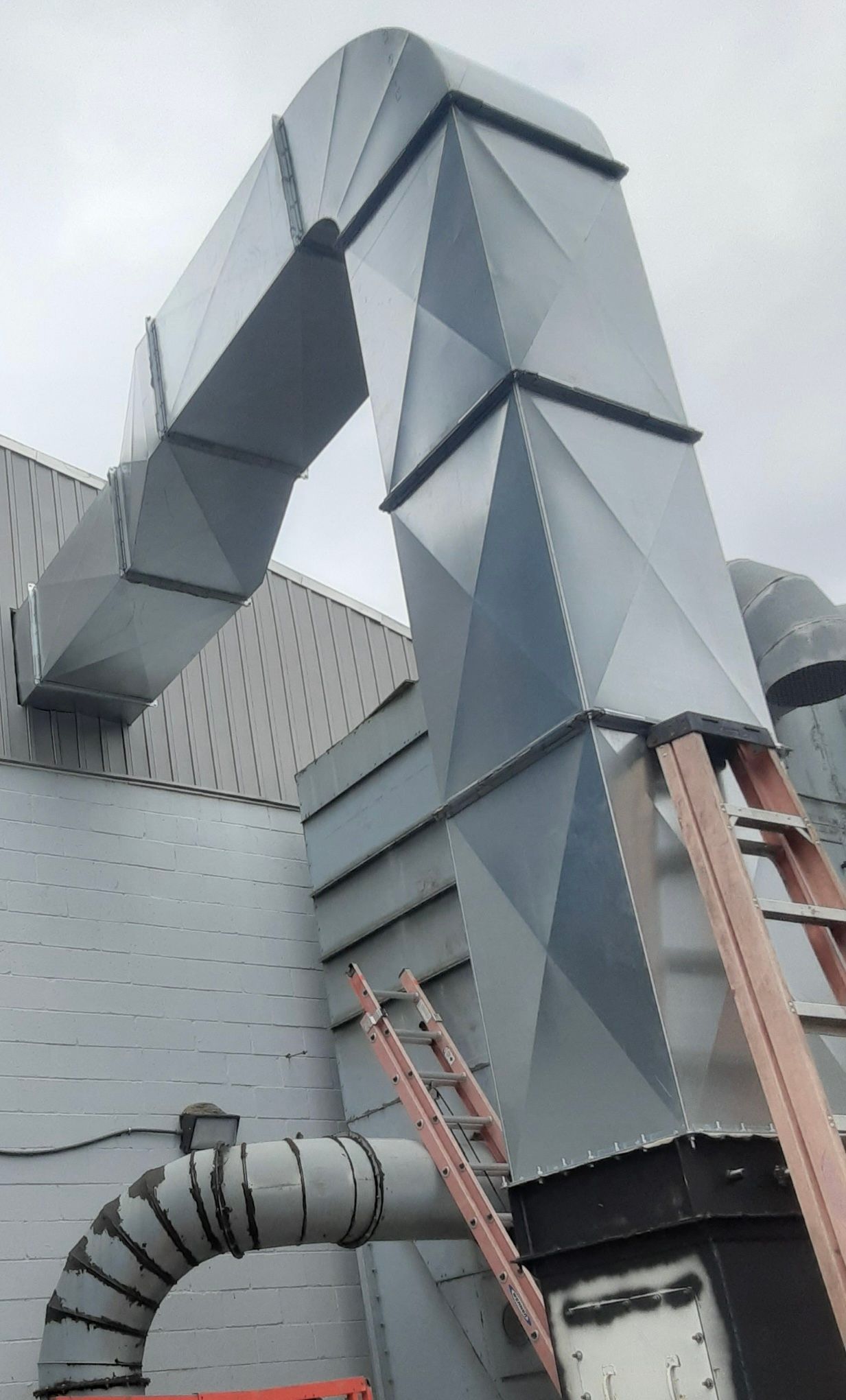 Galvanized metal ductwork on exterior building wall. A ladder leans against the structure.