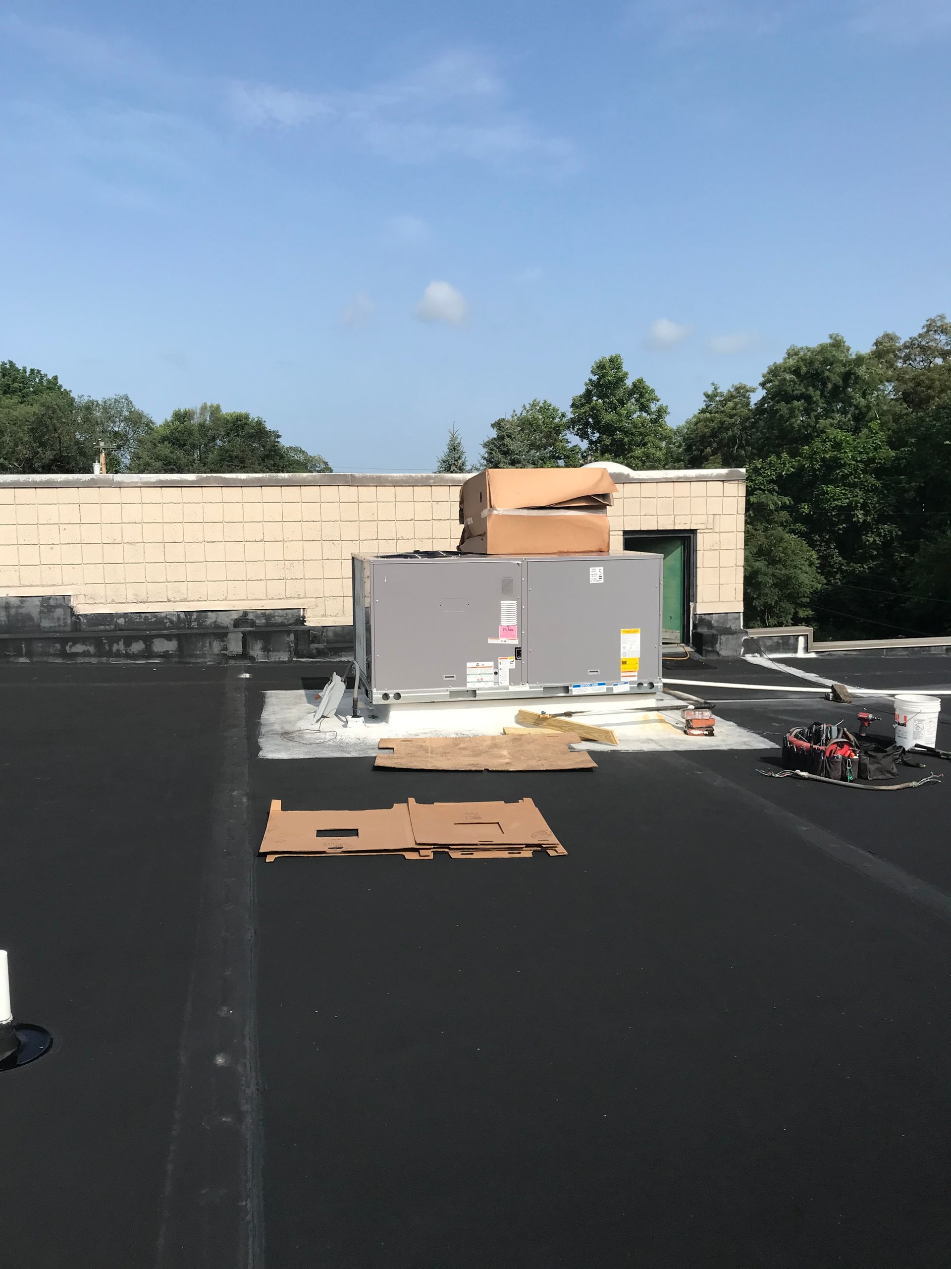 HVAC unit being installed on a flat roof. Cardboard and tools visible. Sunny day.