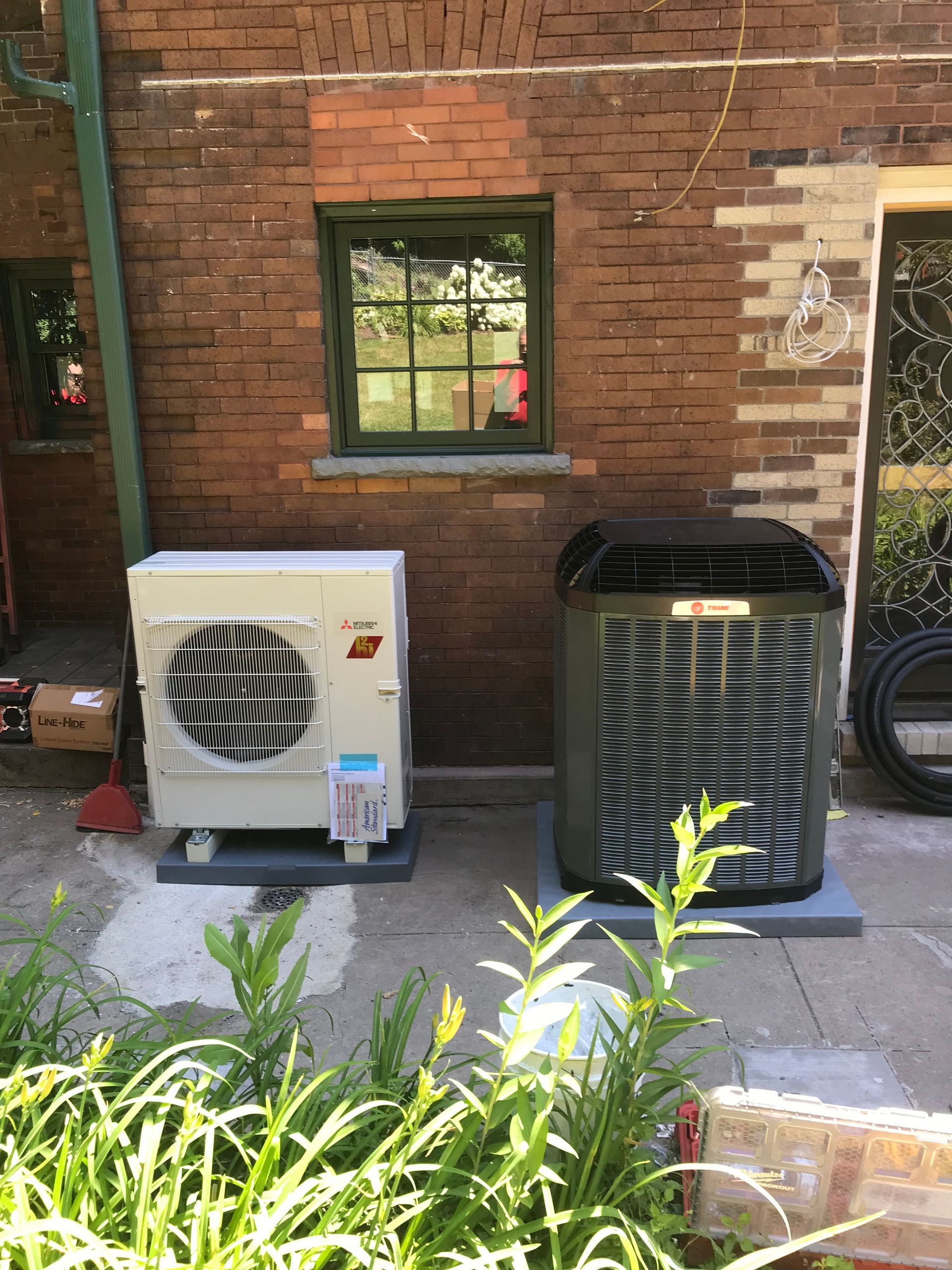 Two HVAC units on concrete pads against a brick building with a window.