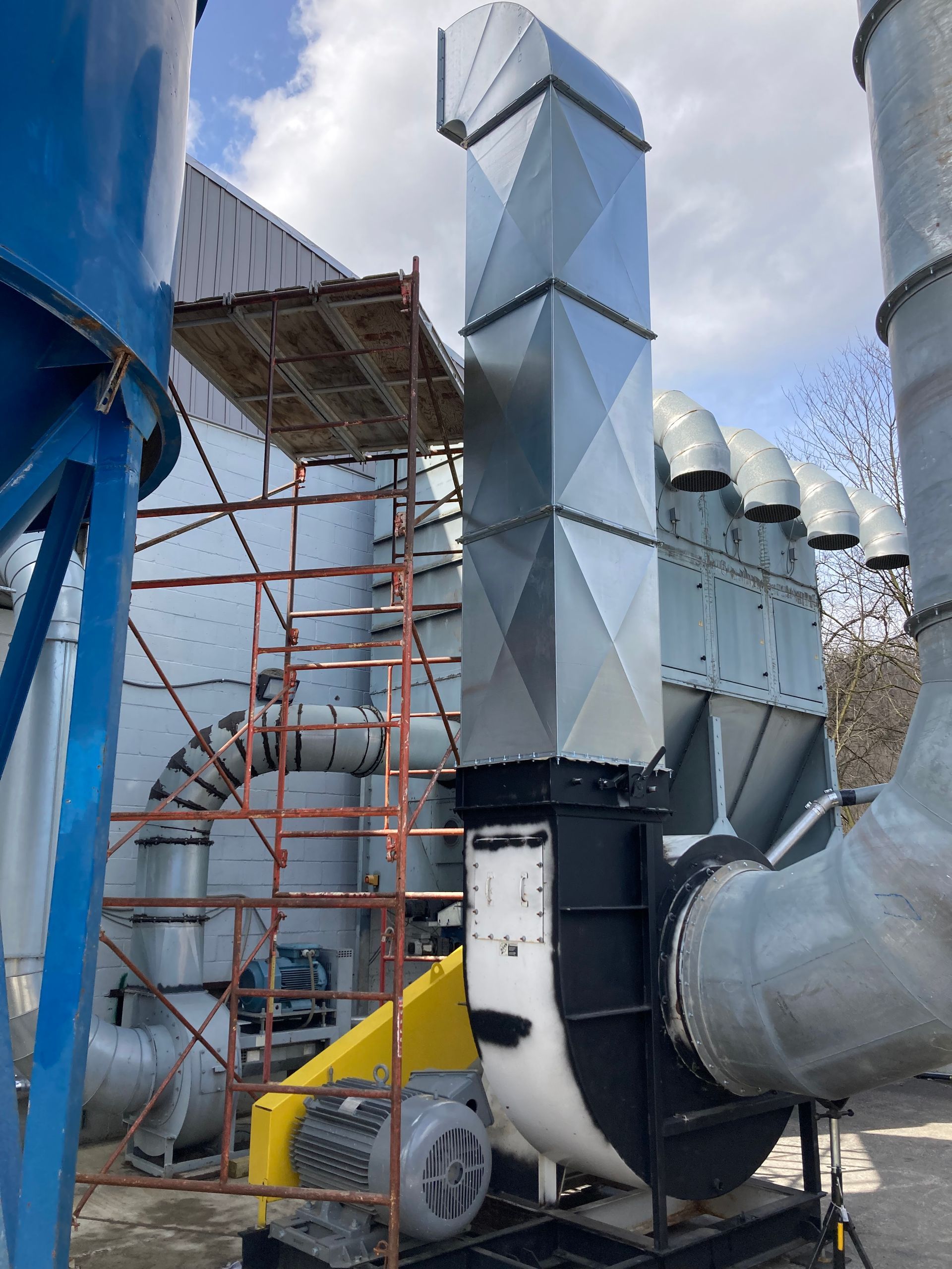 Industrial dust collection system with metal ductwork, blue silo, and yellow fan.