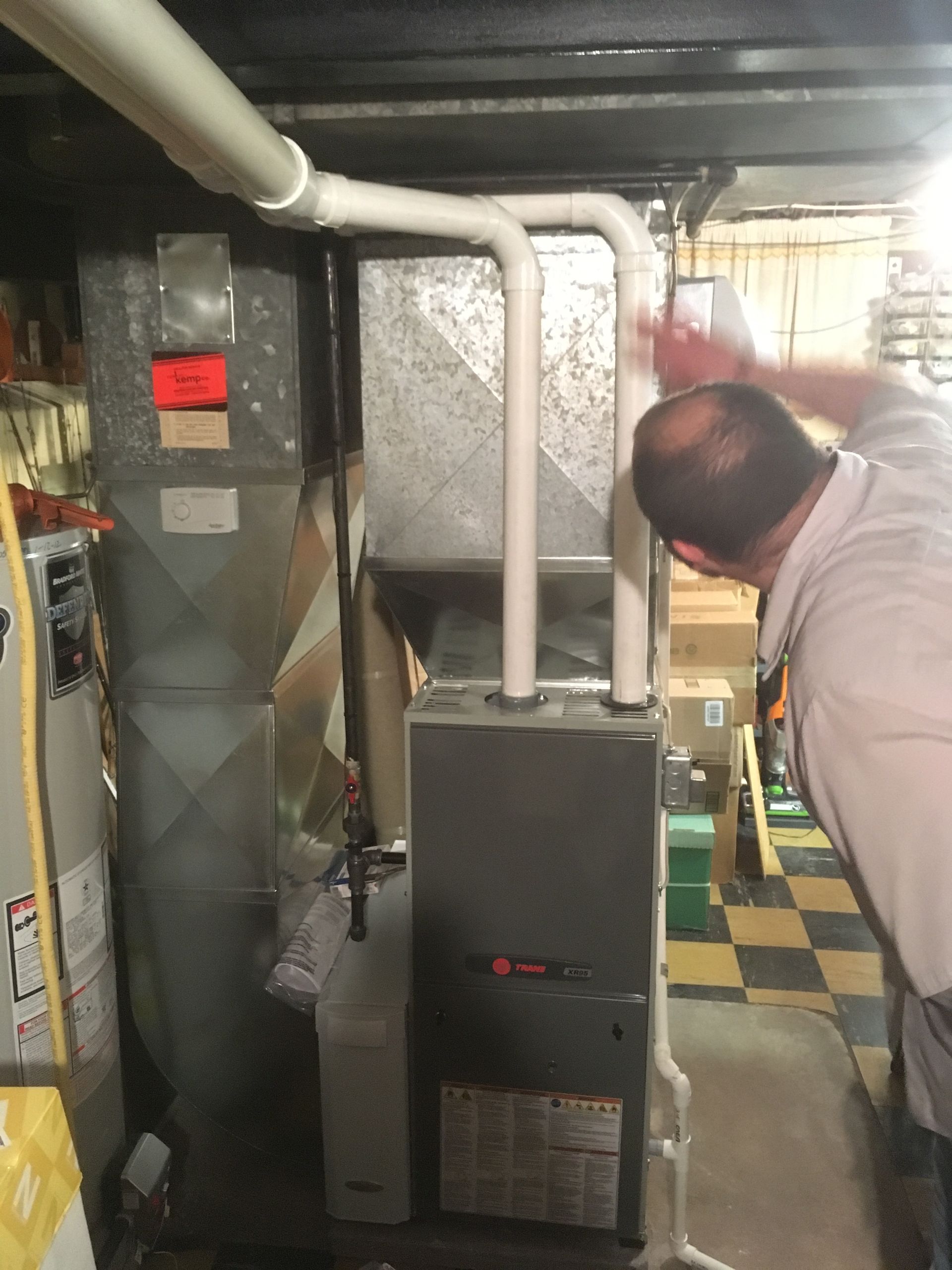 Man inspecting furnace in basement. Furnace is silver and gray, with white pipes.