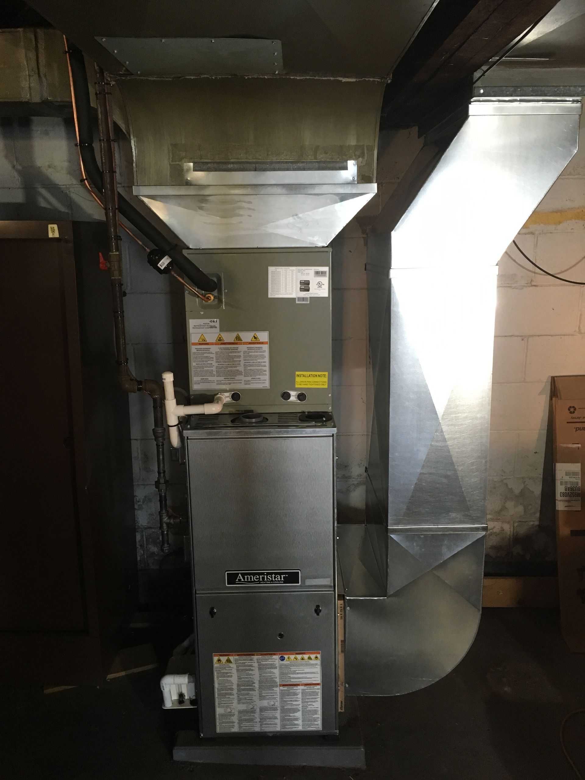 A furnace unit in a basement, with ductwork and pipes, near a door.