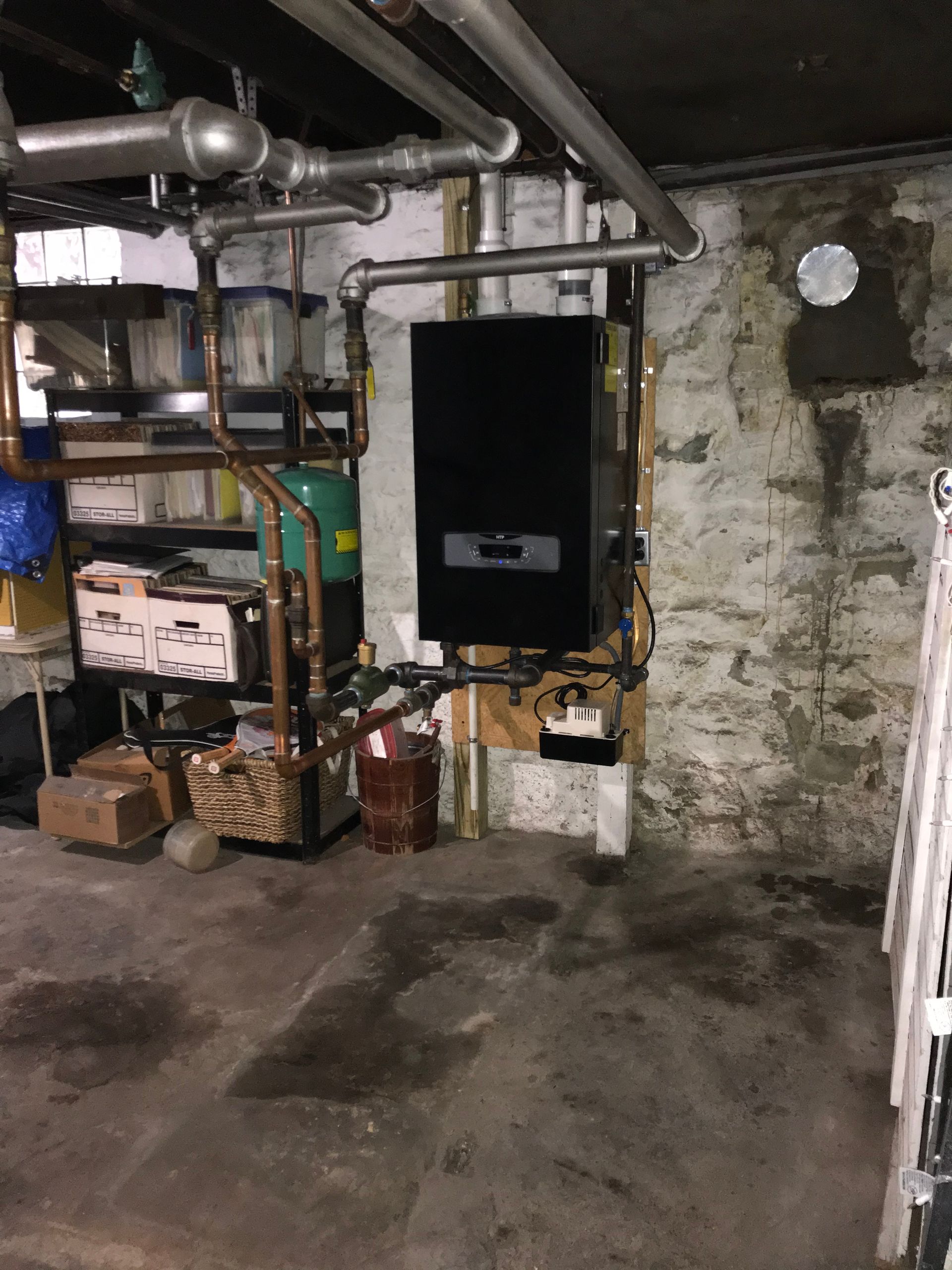 Basement with boiler and pipes; concrete floor and stone wall.