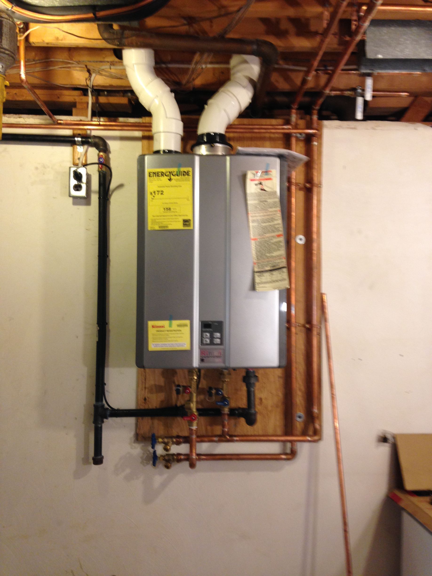 Tankless water heater with copper piping and white vent pipes in a basement.