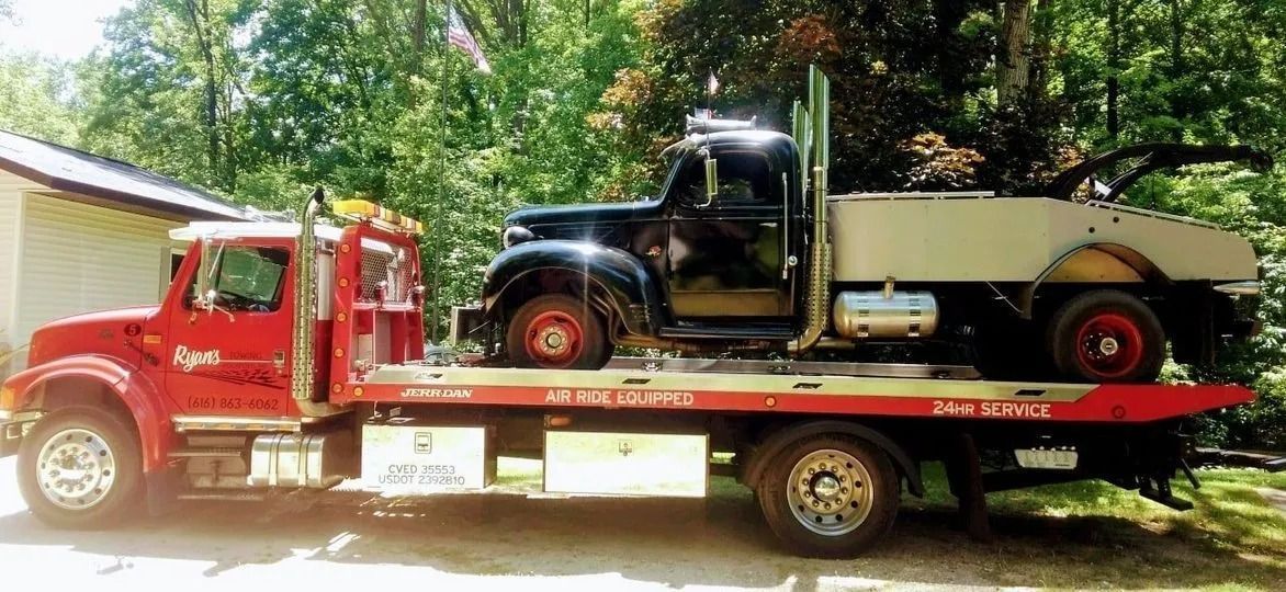 Red flatbed tow truck hauling a vintage black car in a sunny driveway