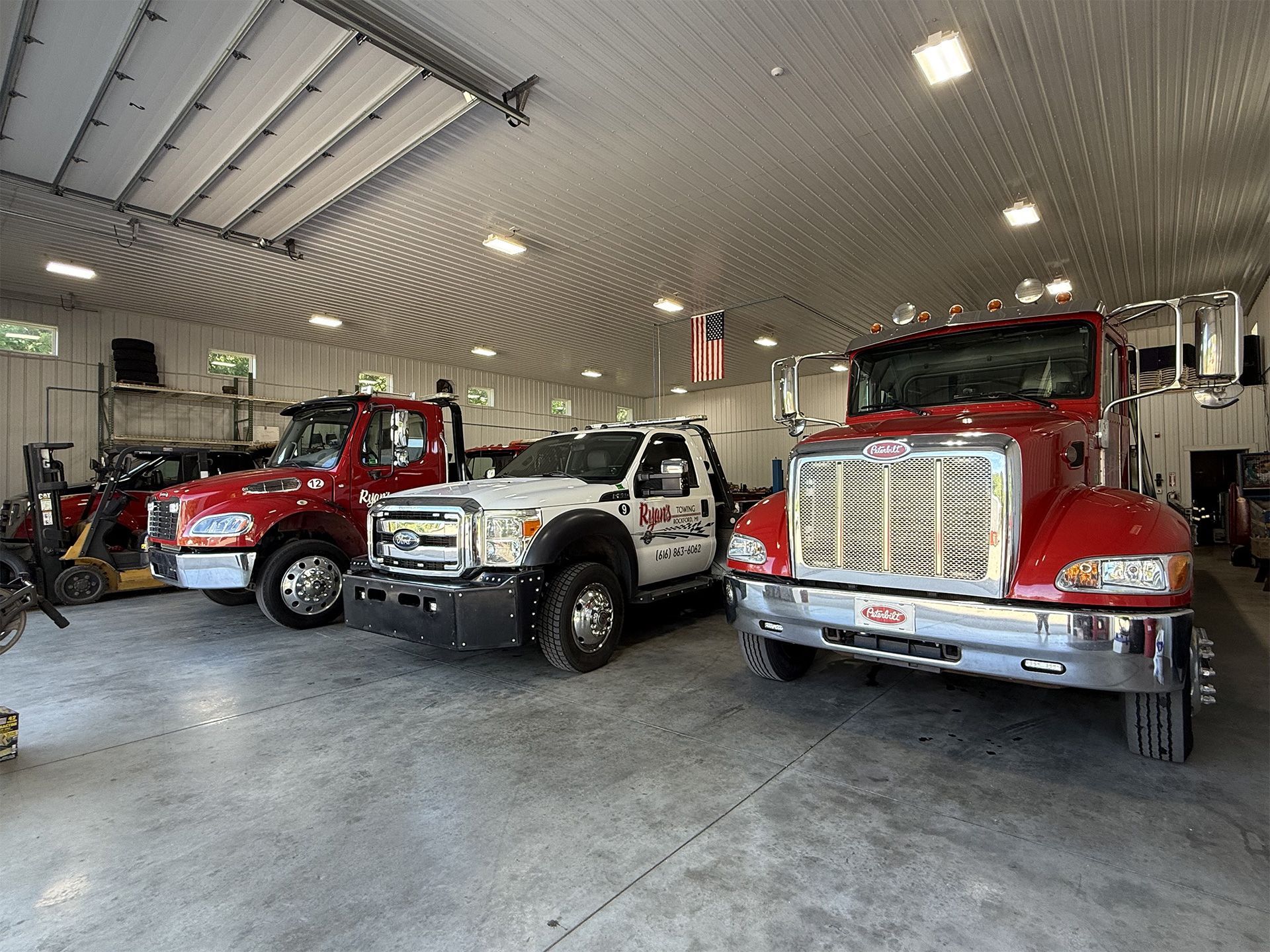 Three fire trucks parked inside a bright garage, including a red truck and a white utility pickup.