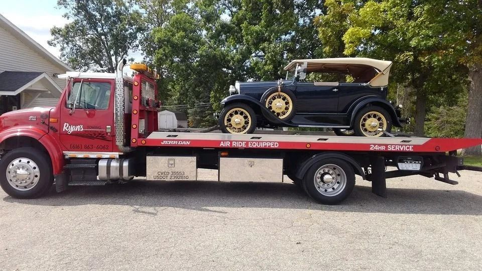Red tow truck carrying a vintage black car on a flatbed roadside.