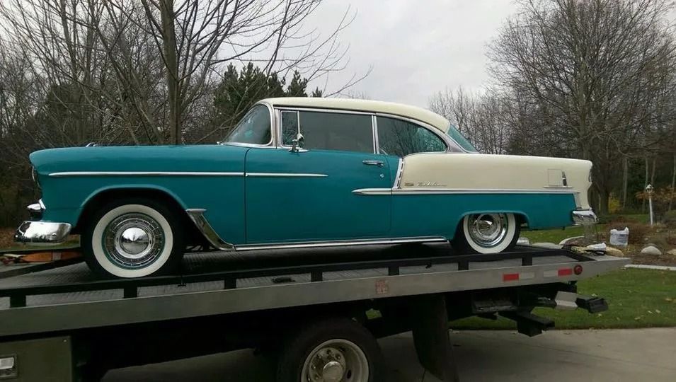 Classic turquoise and cream vintage car on a flatbed trailer outdoors under overcast skies