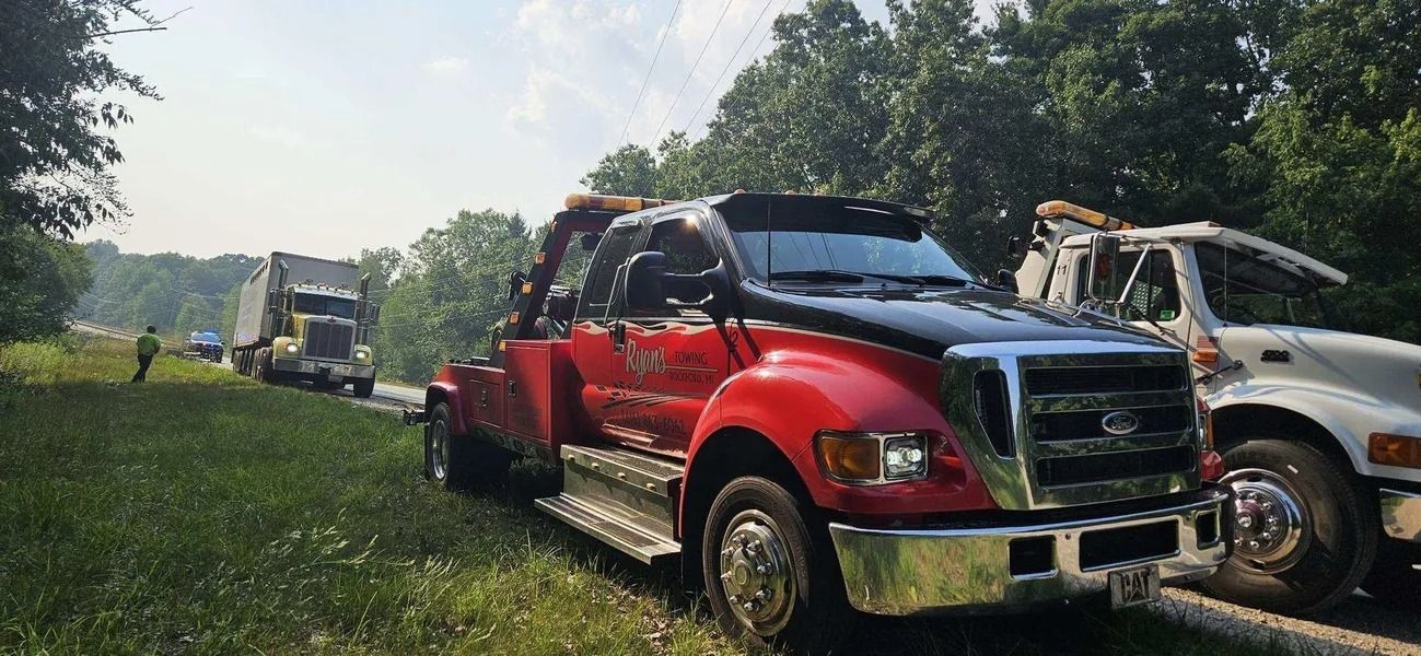 Two tow trucks hauling damaged vehicles along a grassy roadside