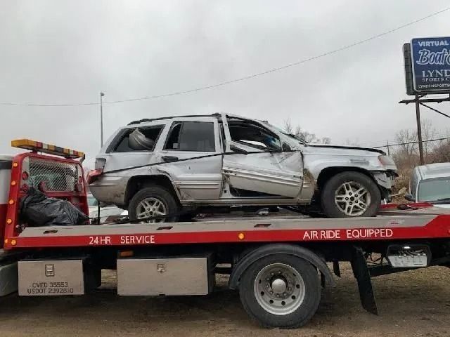 Damaged silver SUV on a tow truck by the roadside in winter.
